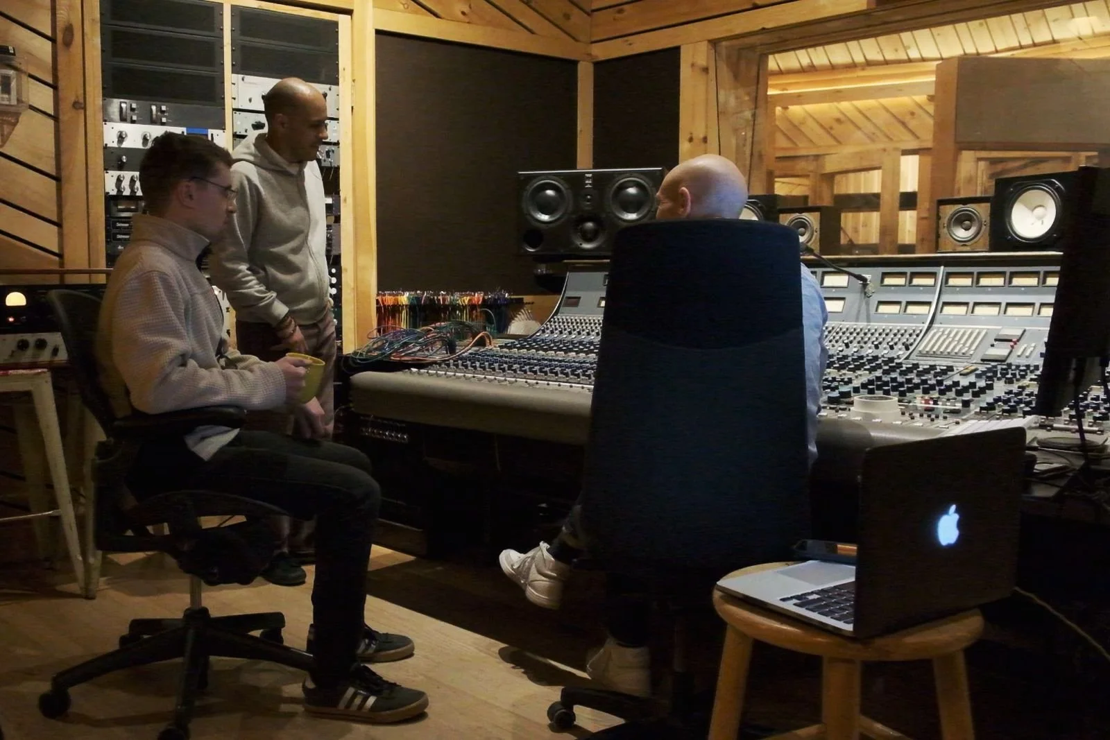 Three people in a music recording studio working with audio equipment and a mixing console.