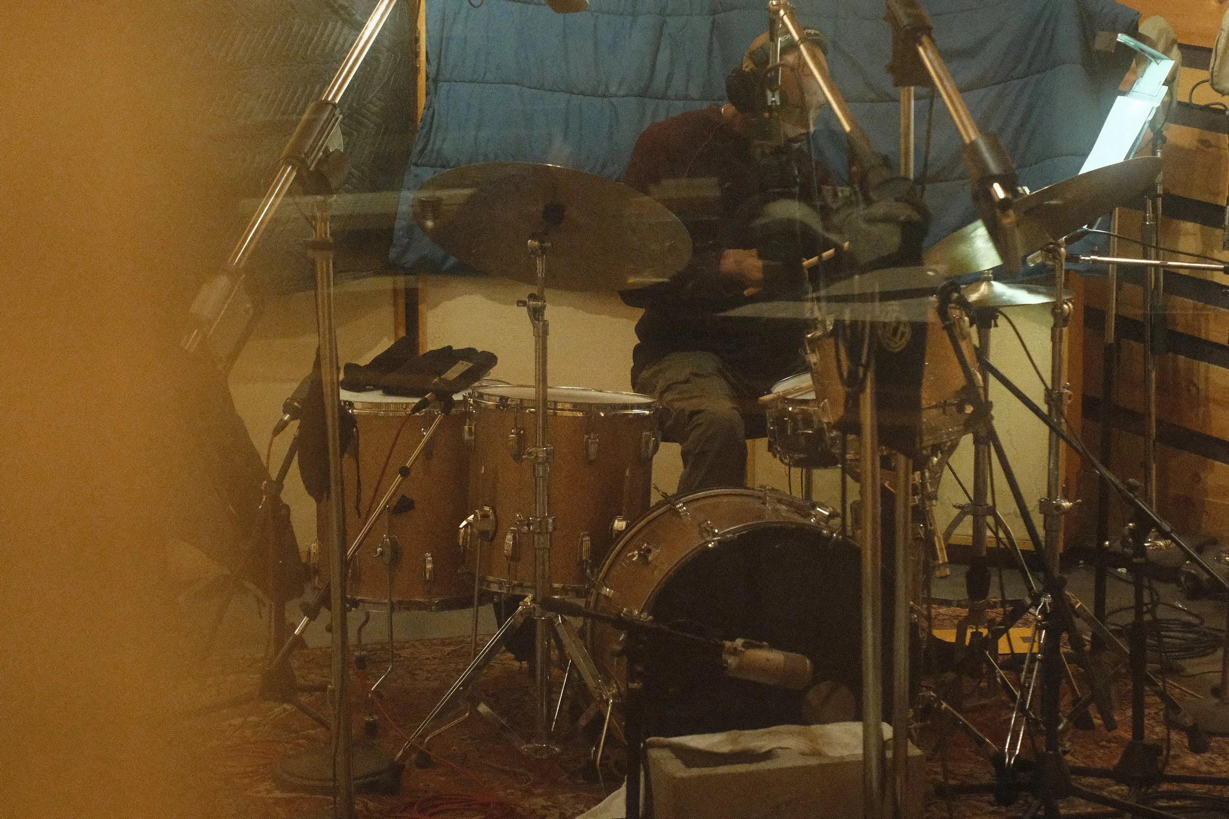Drummer playing in a recording studio with drum kit and microphones.
