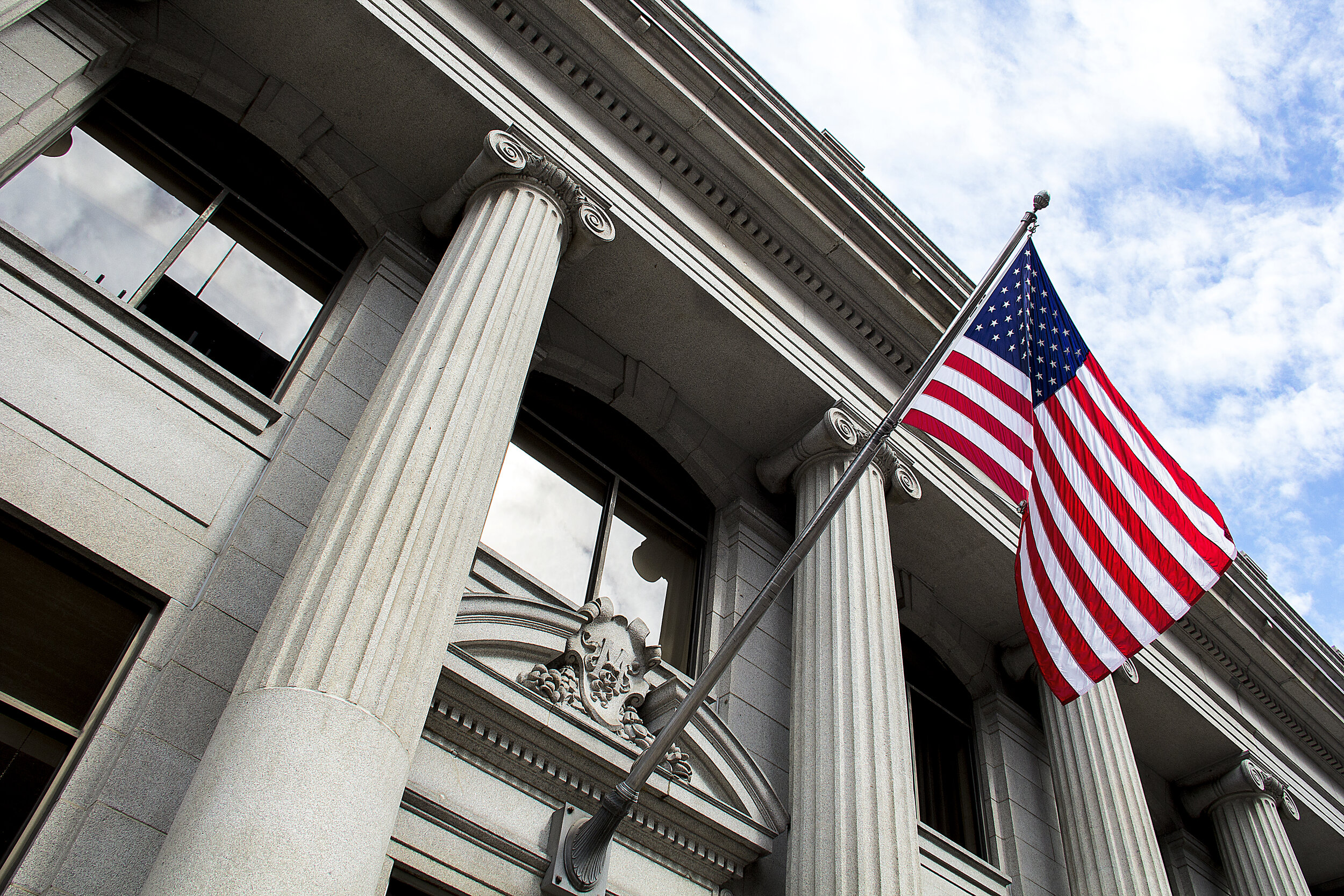 American-flag-flying-over-government-building-in-city,-blue-sky-and-clouds-1263450790_5184x3456.jpeg