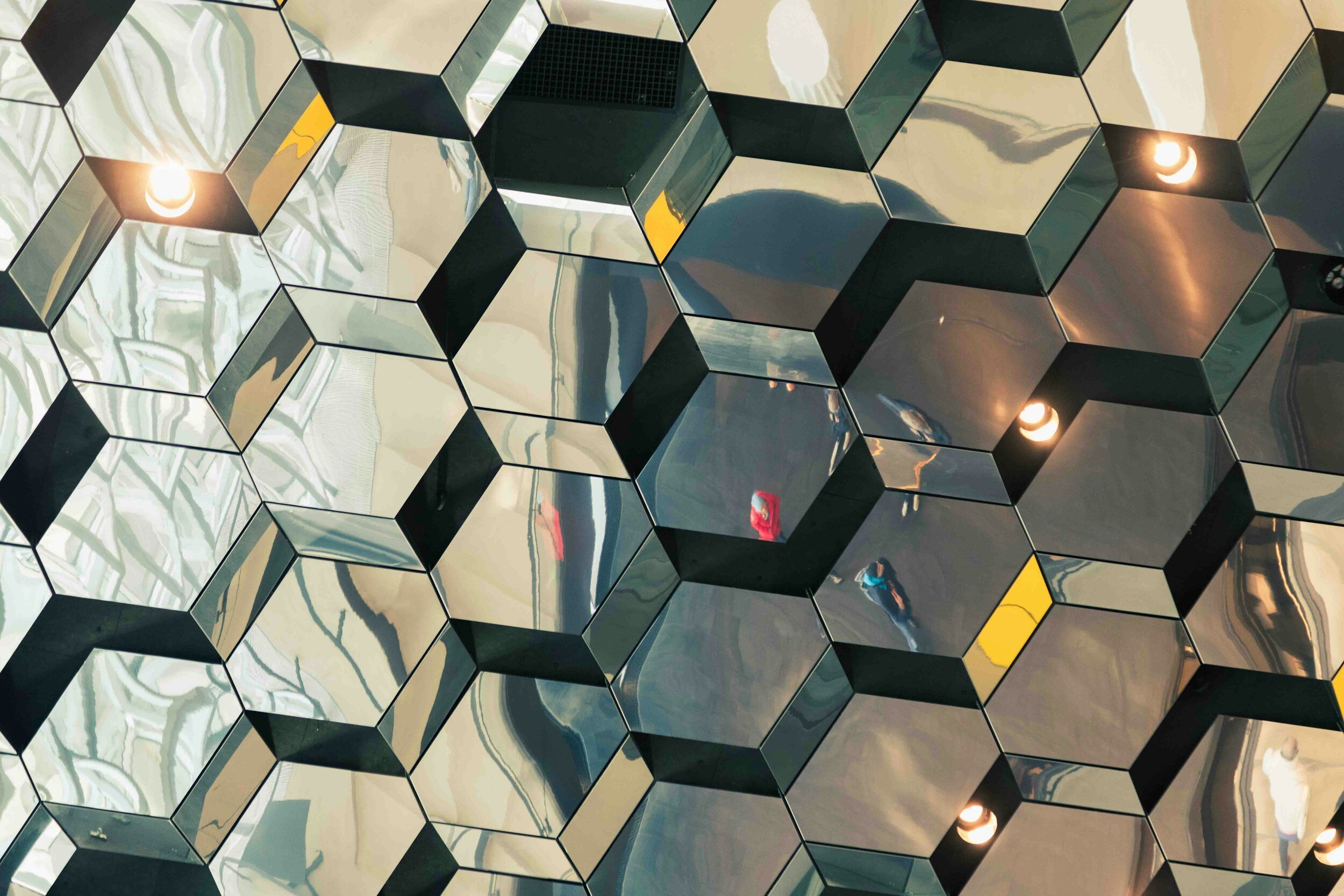 Ceiling with hexagonal mirrored panels reflecting lights and surroundings.