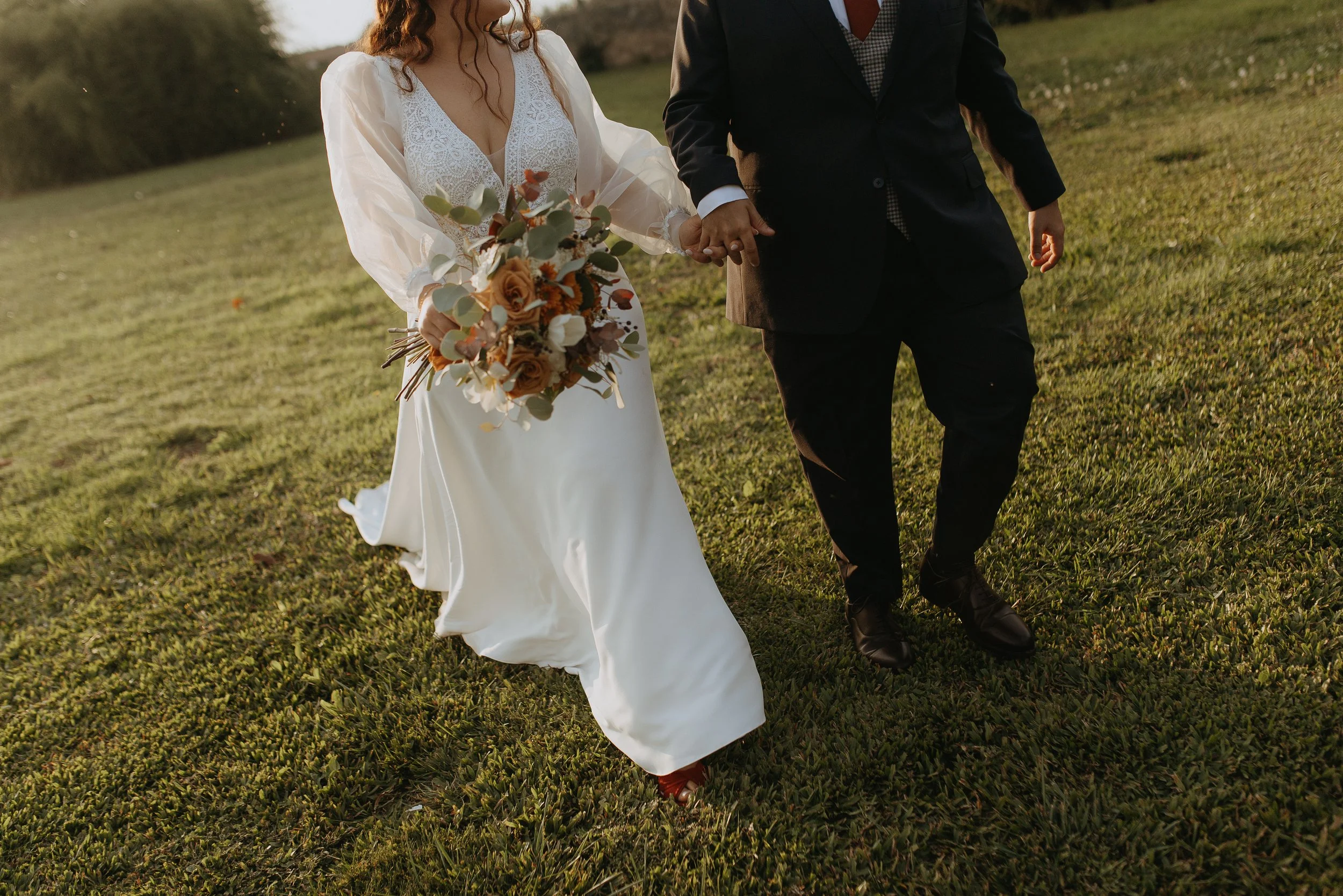 A bride and groom holding hands and walking on a grassy field during their wedding celebration.