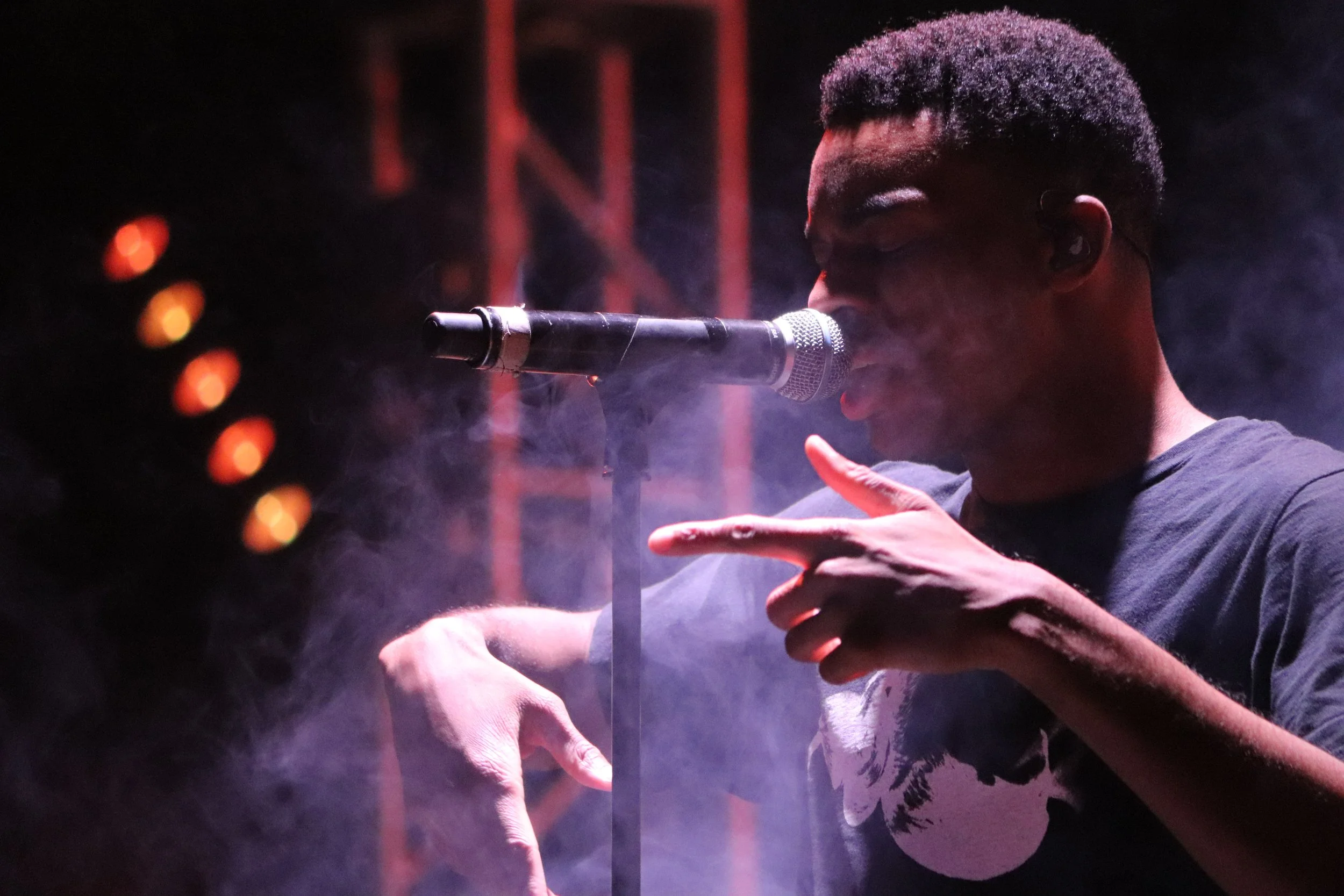 Singer performing on stage with circular patterned backdrop and dim lighting.