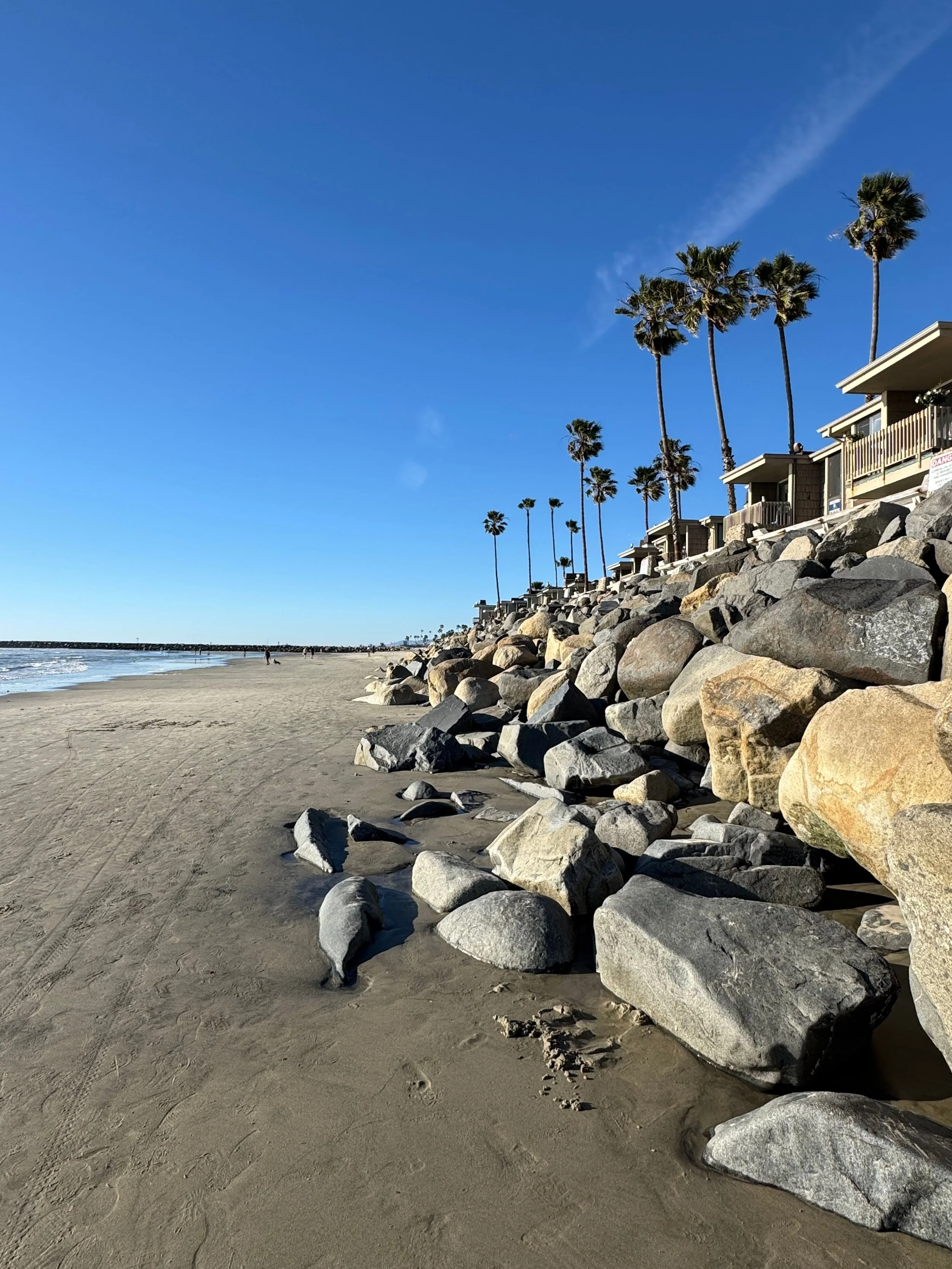 Breakwater Way Beach on a sunny day featuring rocks and palm trees.