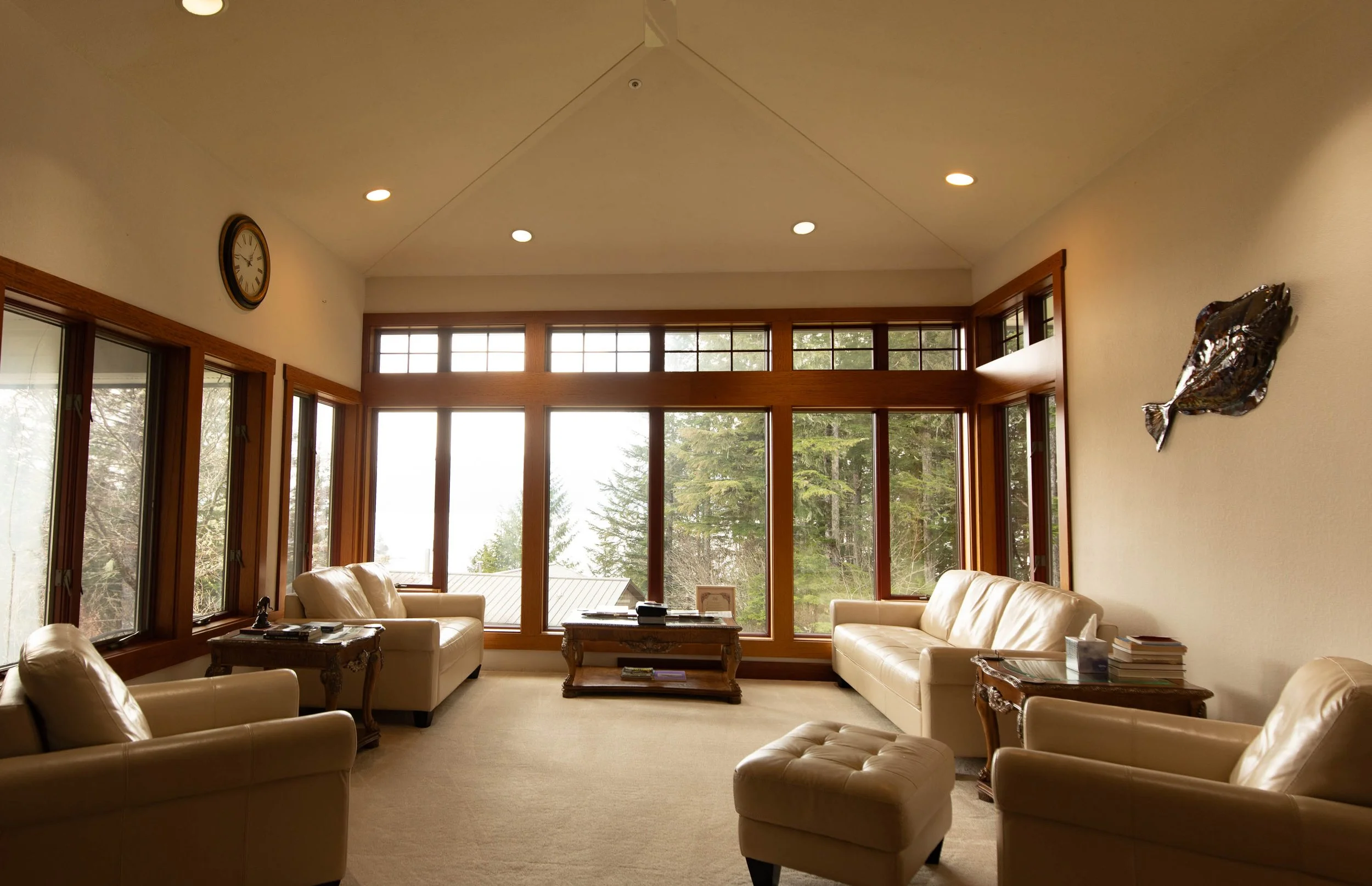 Main living room of Chrome Chasers fishing lodge in Wrangell Alaska featuring floor-to-ceiling tigerwood-framed windows overlooking the Tongass National Forest, vaulted ceiling, and leather furnishings