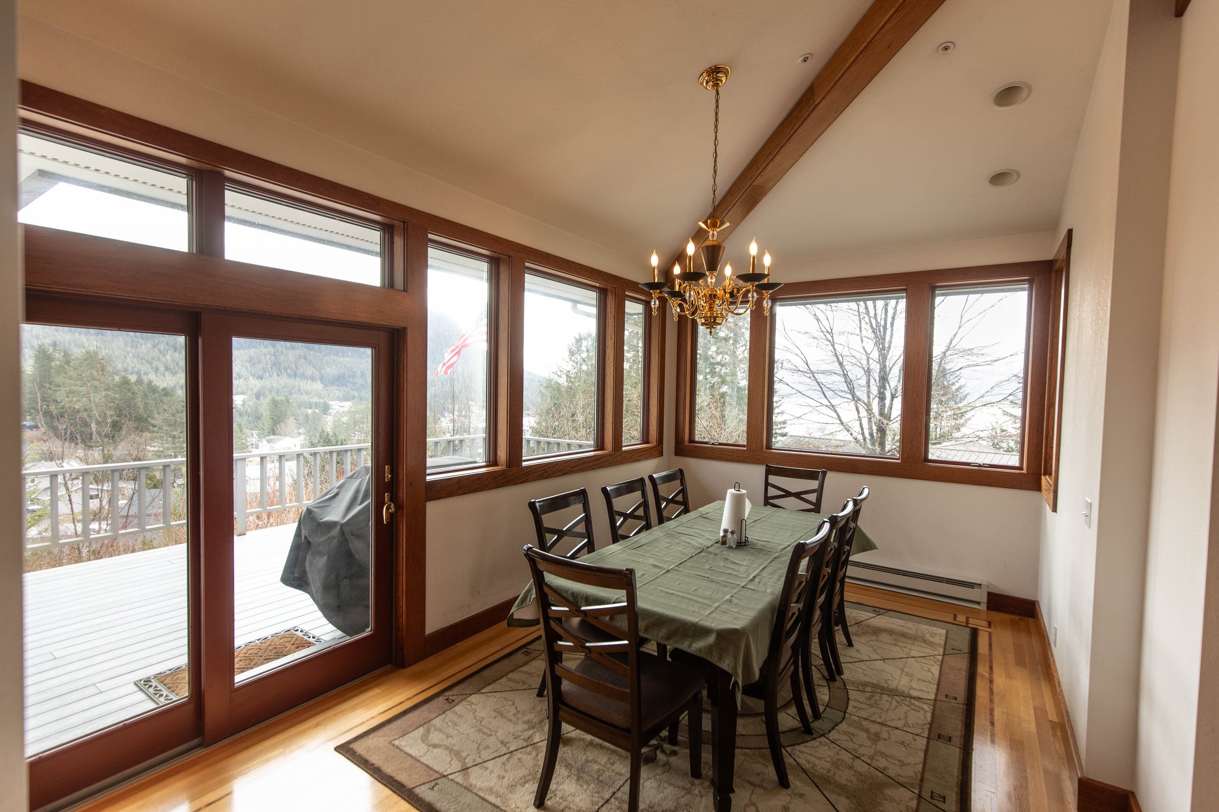 Chrome Chasers lodge dining room in Wrangell Alaska with floor-to-ceiling windows framing the harbor view, Brazilian tigerwood trim, brass chandelier, and table set for guests
