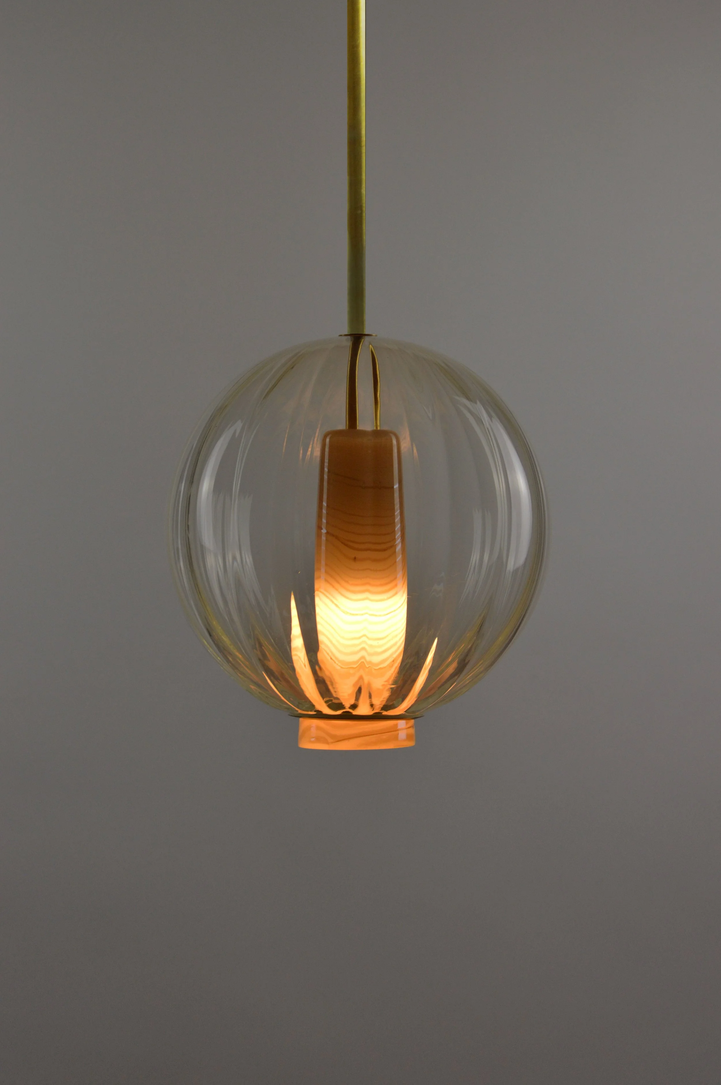 Globe Pendant is an handcrafted pendant light featuring a ribbed colored glass globe surrounding an opalescent glass diffuser with an elegant marbled pattern.