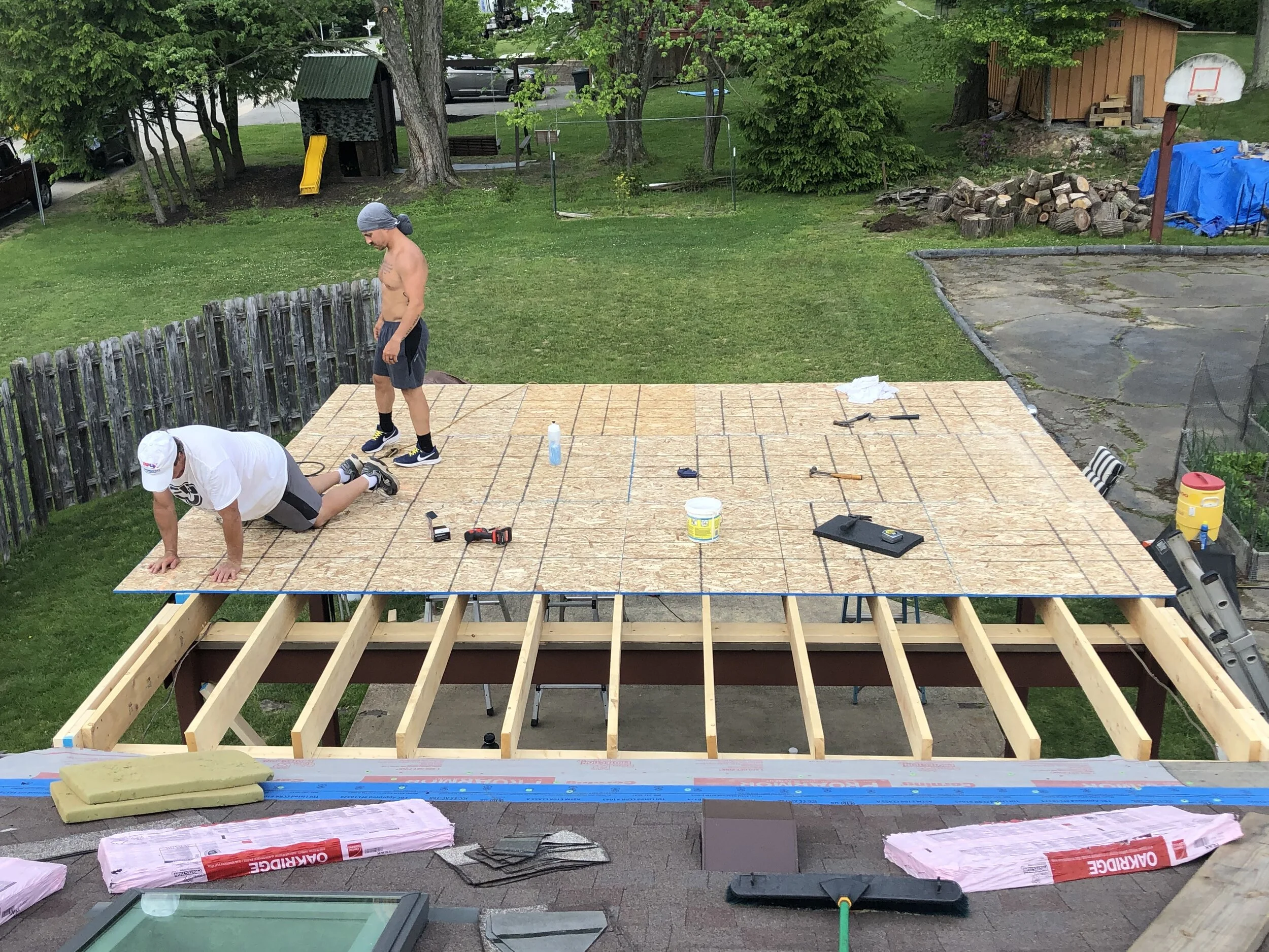 A man and a young boy working on construirunning a house porch or deck in a backyard, with tools, insulation, and building materials around them.