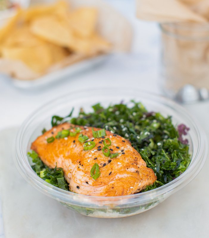 grilled salmon on top of a kale salad with a plate of potato chips in the background