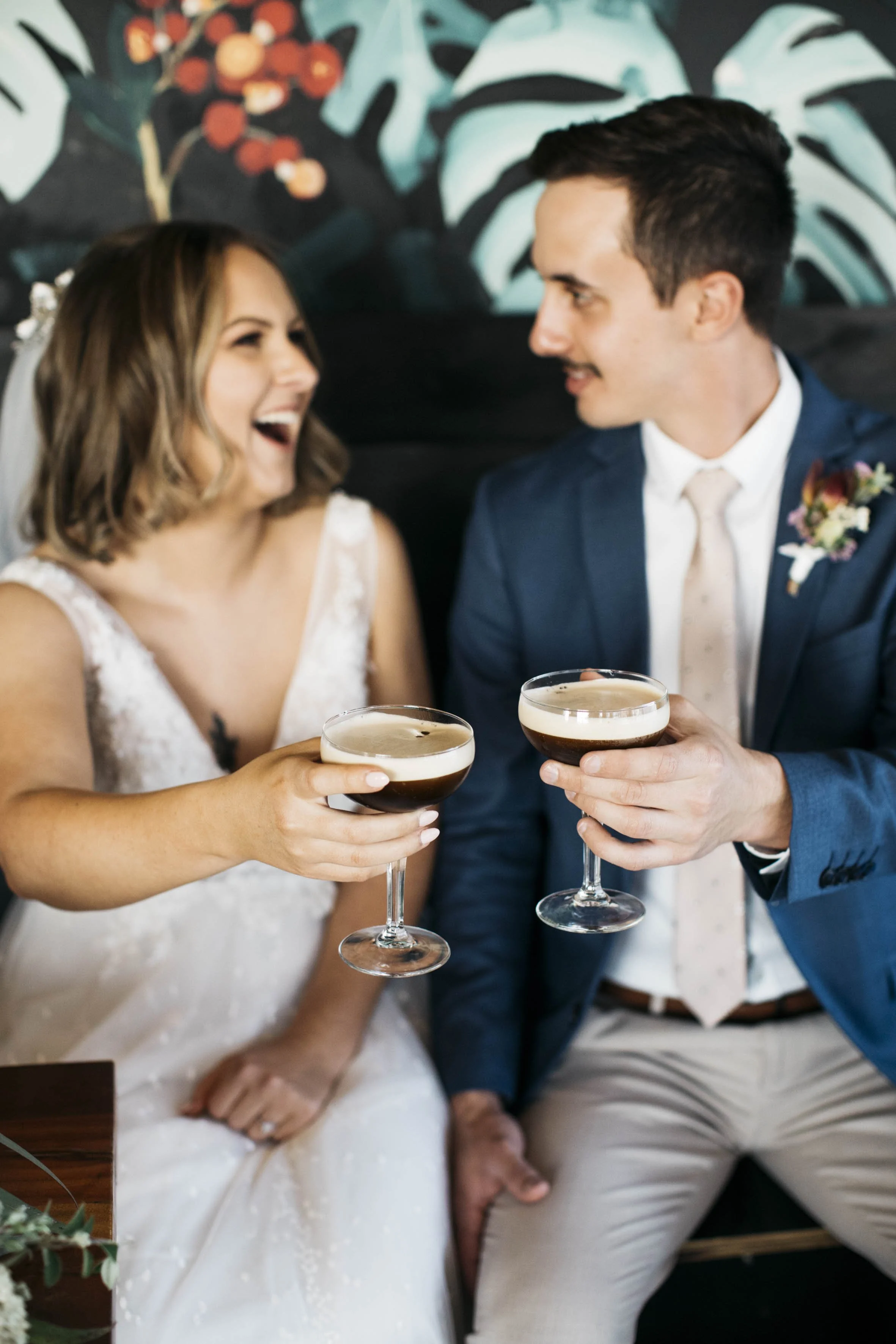 A bride and groom clinking glasses and laughing during their wedding celebration.