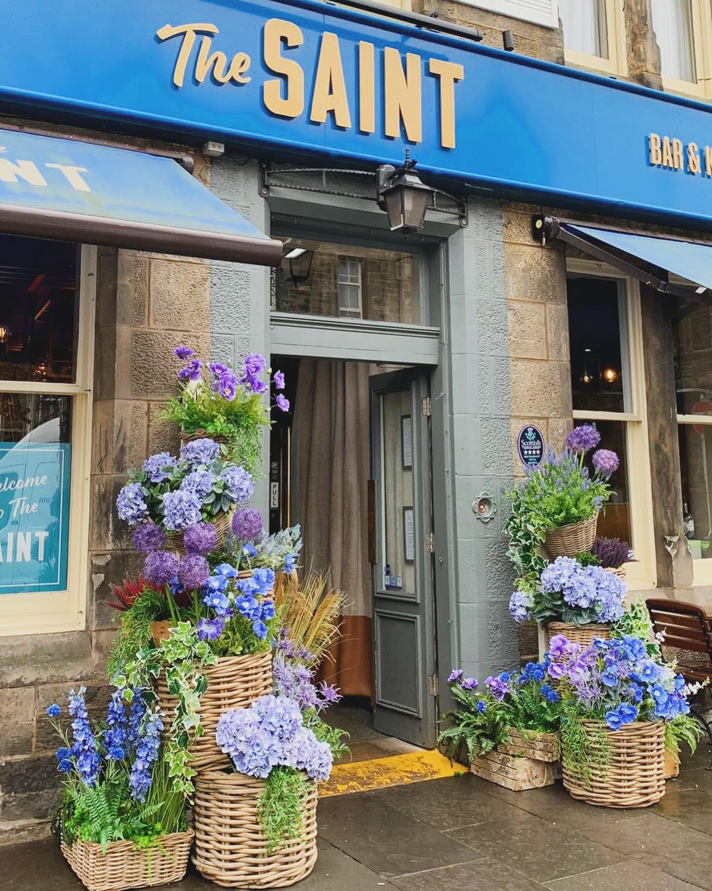 Wicker baskets filled with summer blooms welcomes you to The Saint Bar &amp; Kitchen in St Andrews 🩵🪻