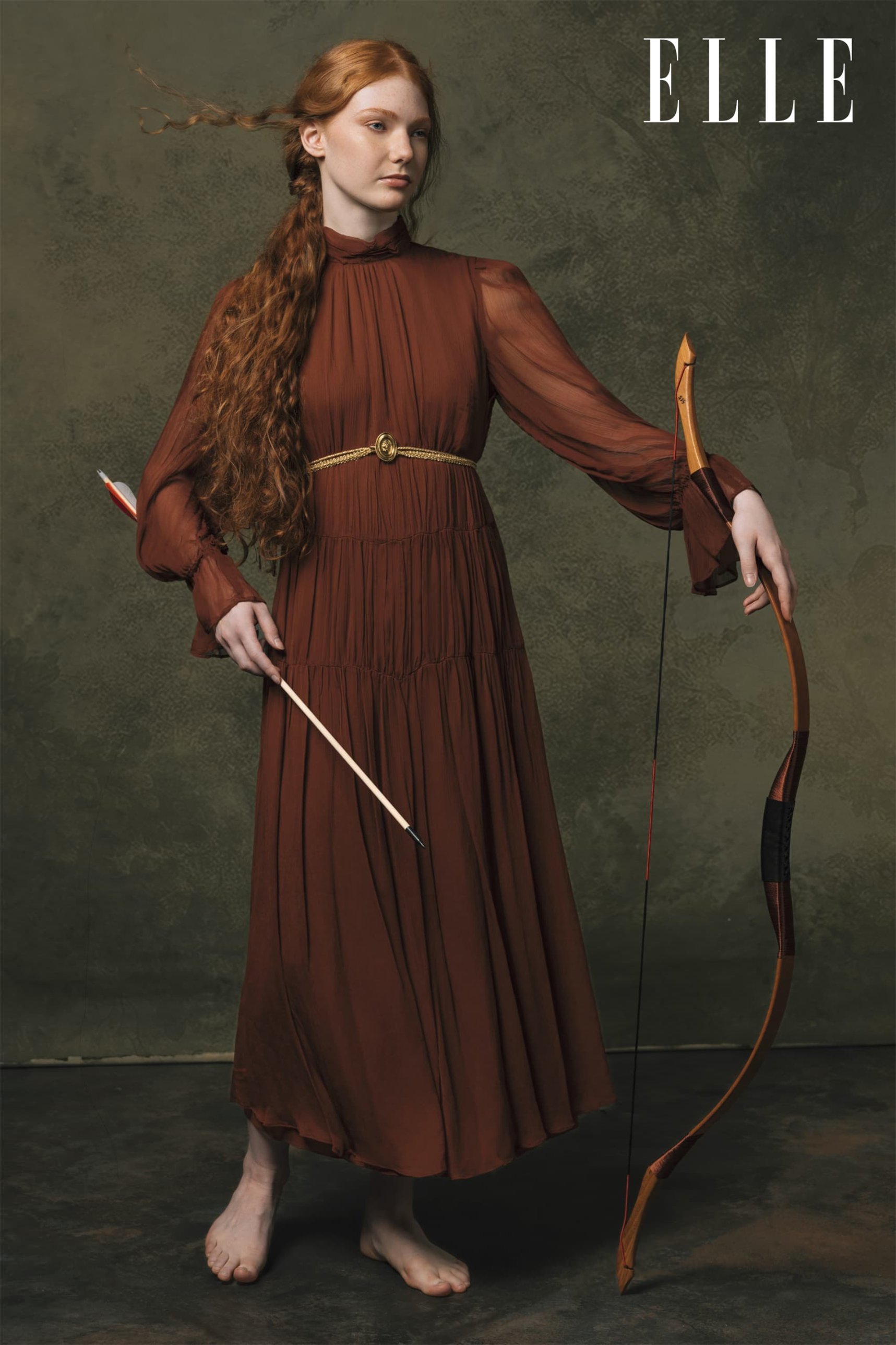 Diana a figura intera con arco e freccia, abito color ruggine e cintura dorata. Chasing Myths di Alessandro Giugni per ELLE Uzbekistan
