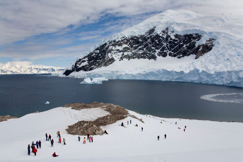 Tourists dressed in red jackets exploring a snow-covered landscape near the Antarctic coast.