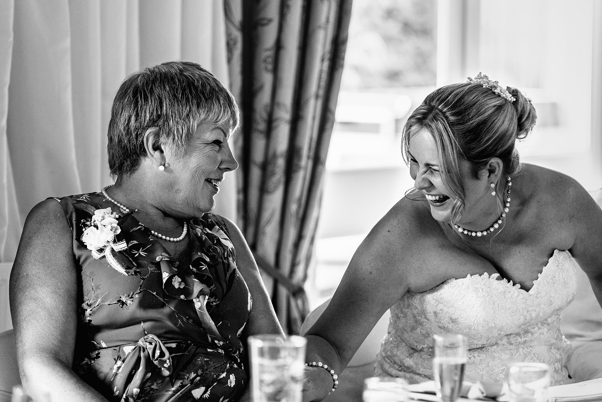  A bride and her mother laughing during wedding reception speeches 