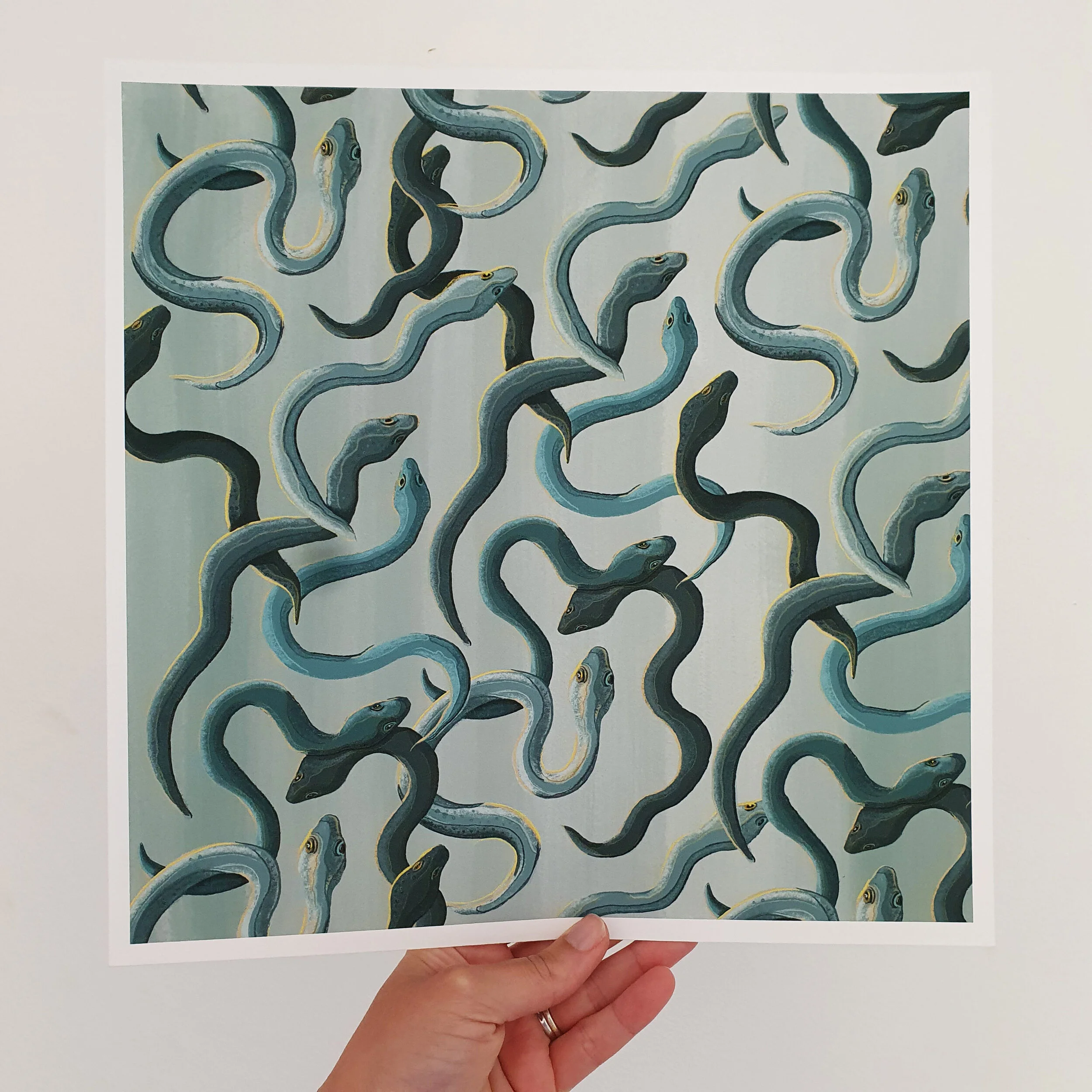 elvers, young eels in varying shades of turquoise and yellow swim across a watery blue background. Giclée print of digital illustration held up by hand against white background.