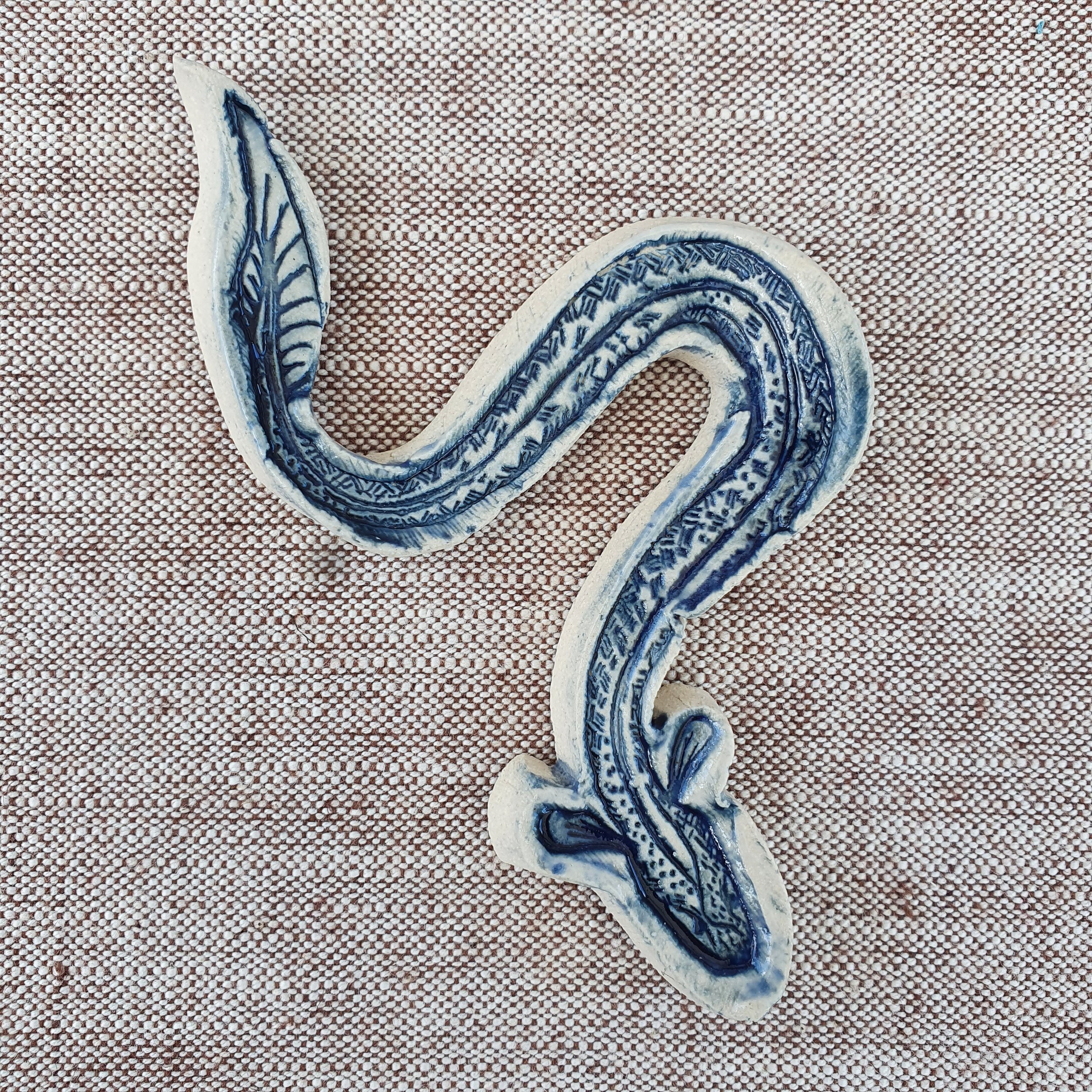 Ceramic eel glazed in dark blue lays on a linen table cloth.