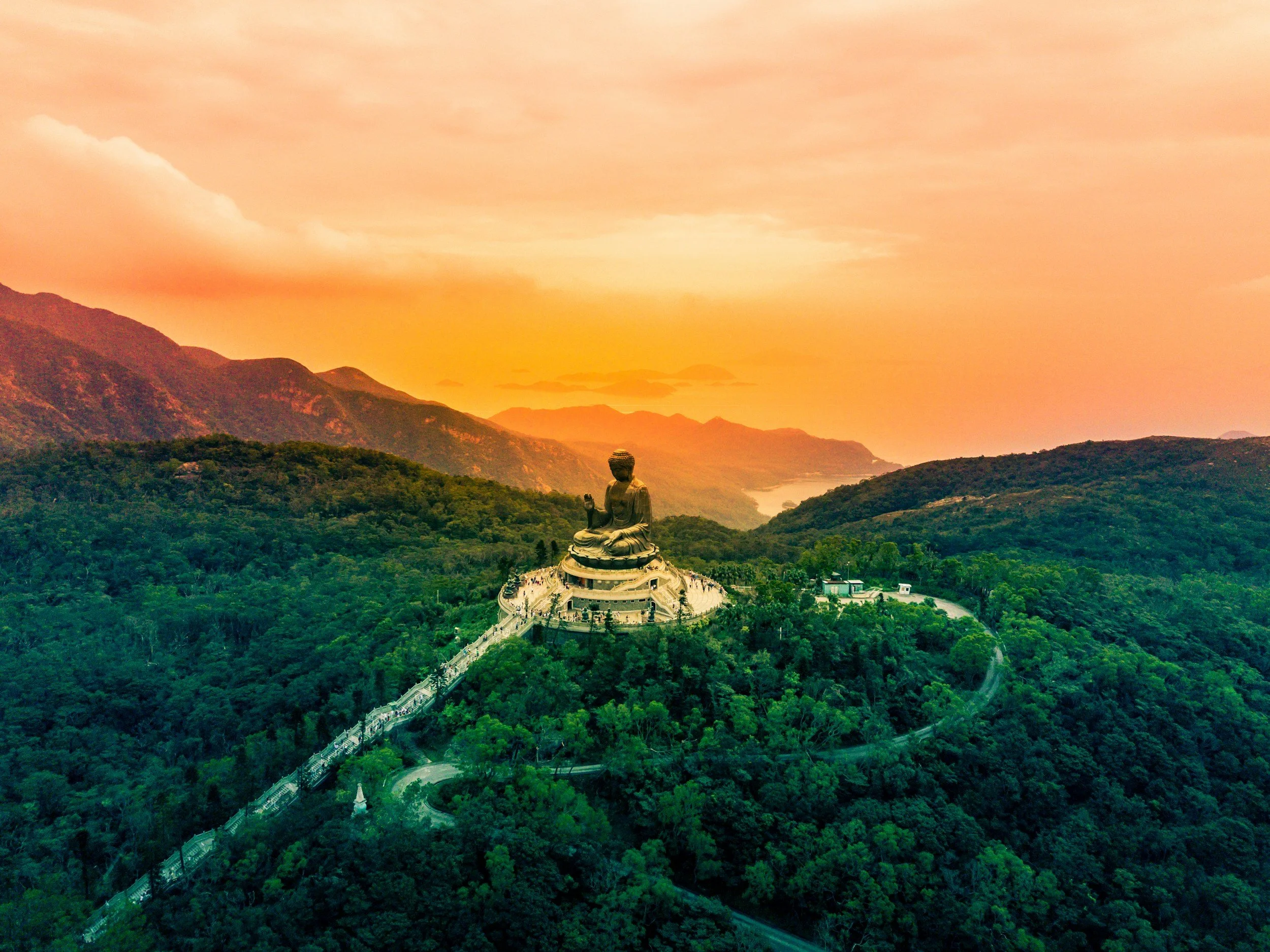A large golden Buddha statue overlooking a lush green valley and mountains during a sunset.