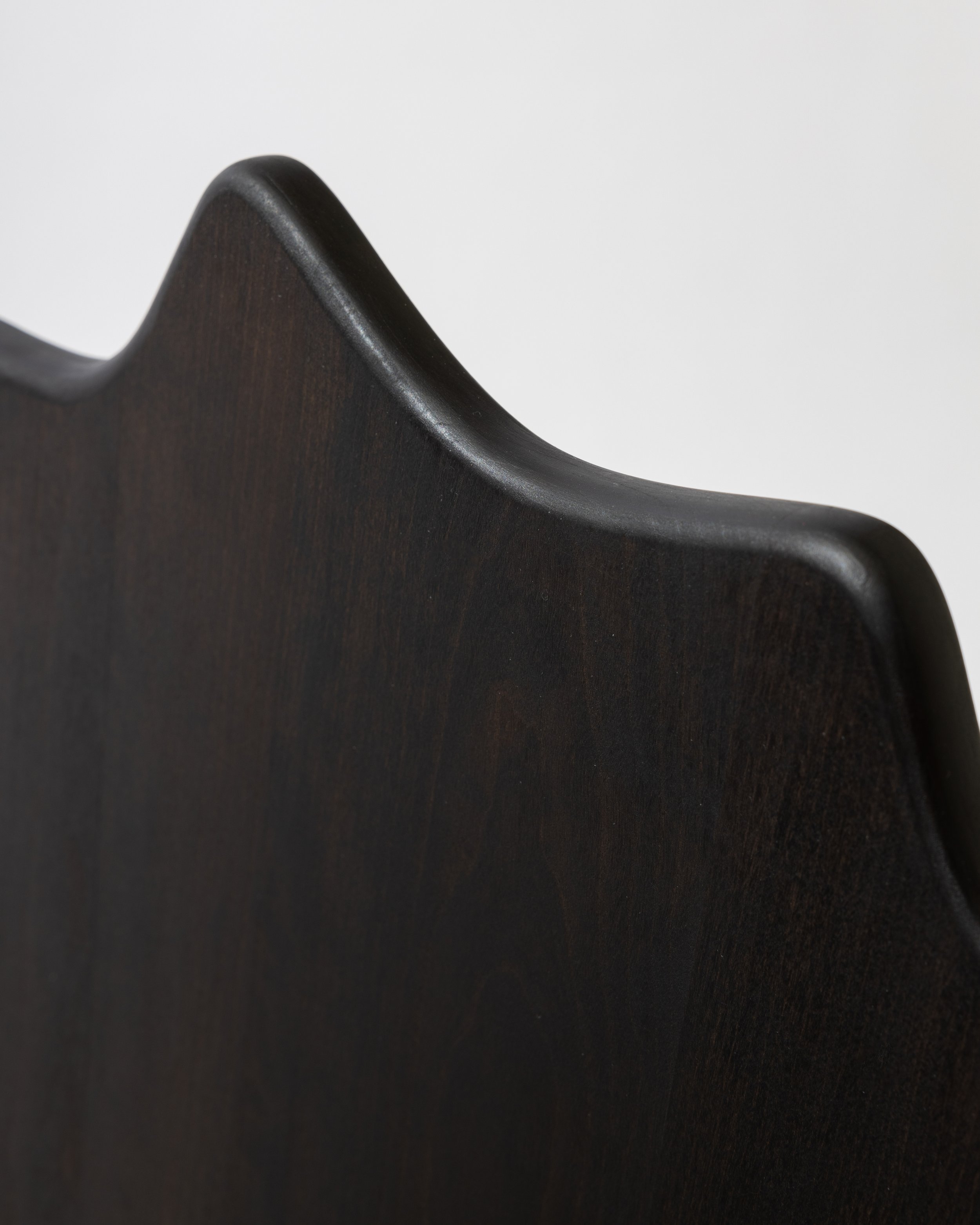 Close-up of the curved edge of a dark, polished wooden surface against a plain light gray background.