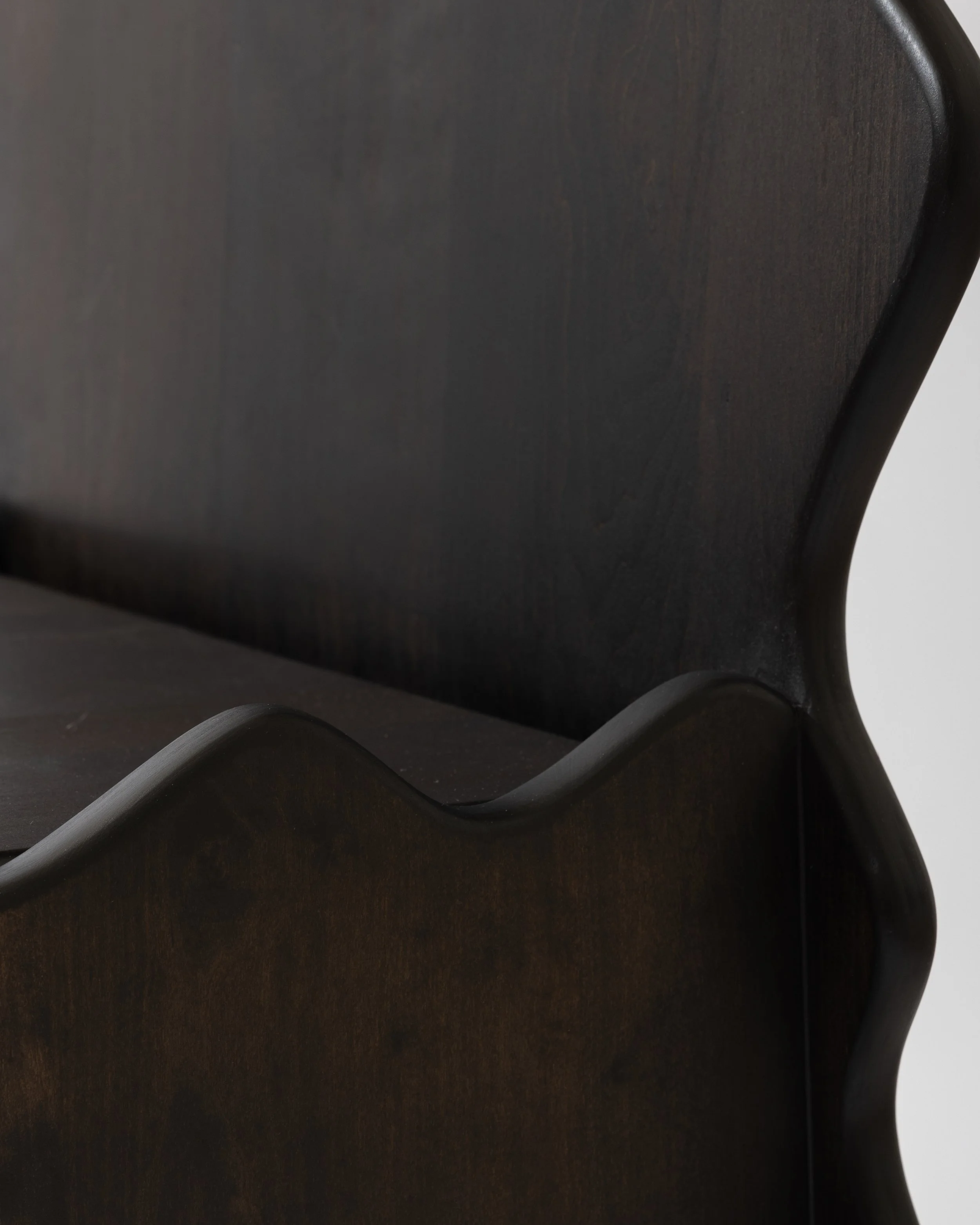 Close-up of a dark wooden piece of furniture with a curved leg and a rounded corner.