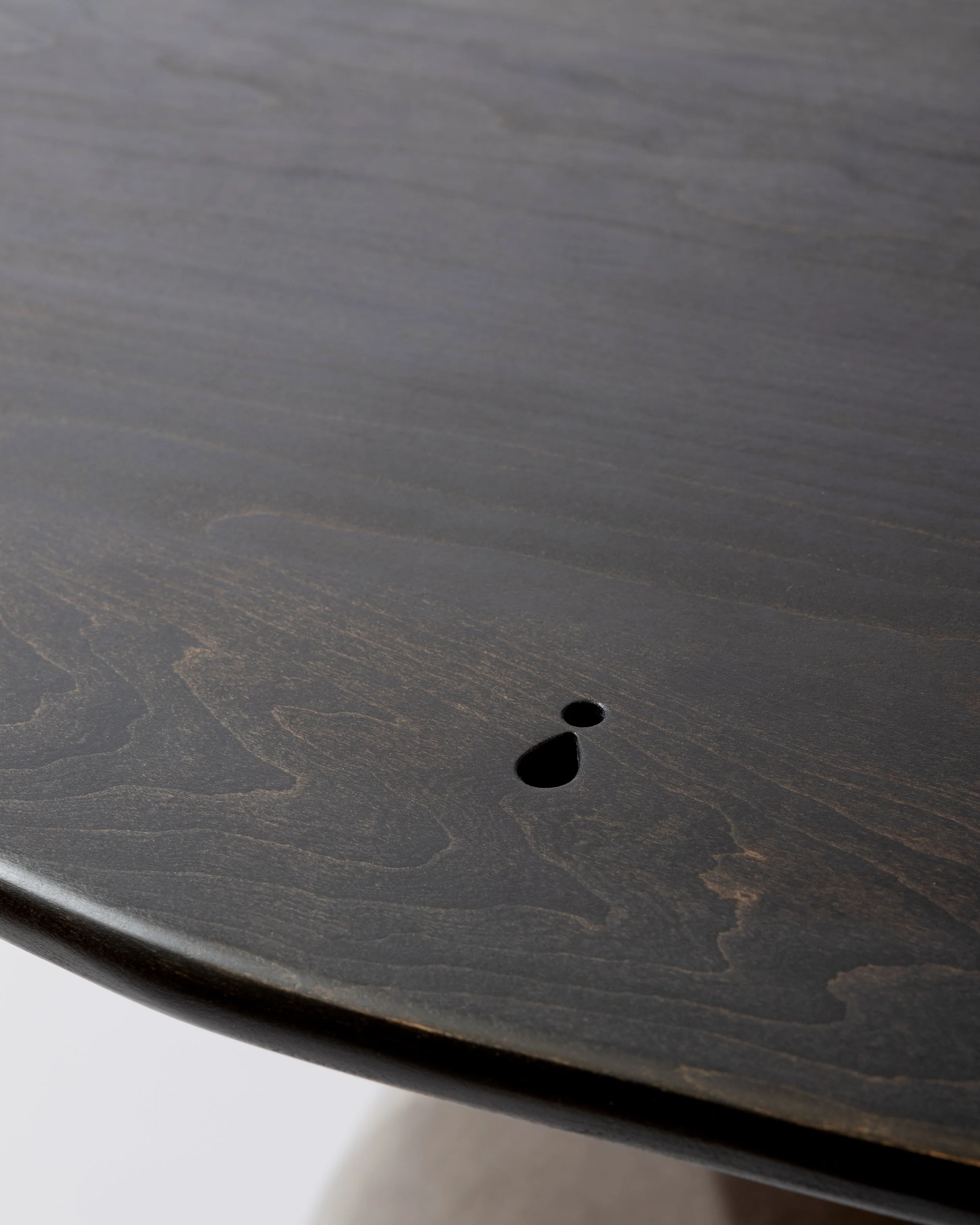 Close-up of a dark wooden surface with a small round hole and smooth curved edges.