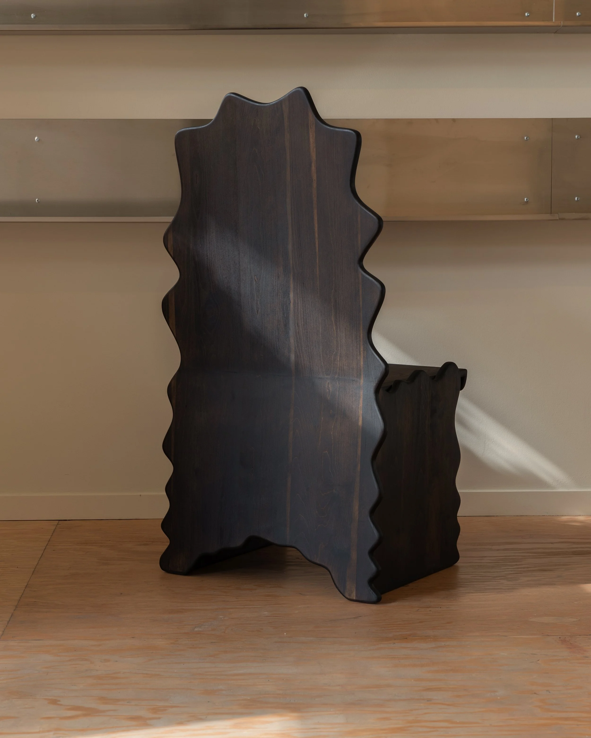Dark wooden chair with a crown-shaped backrest indoors against a wood-paneled wall and a beige stripe on the wall.