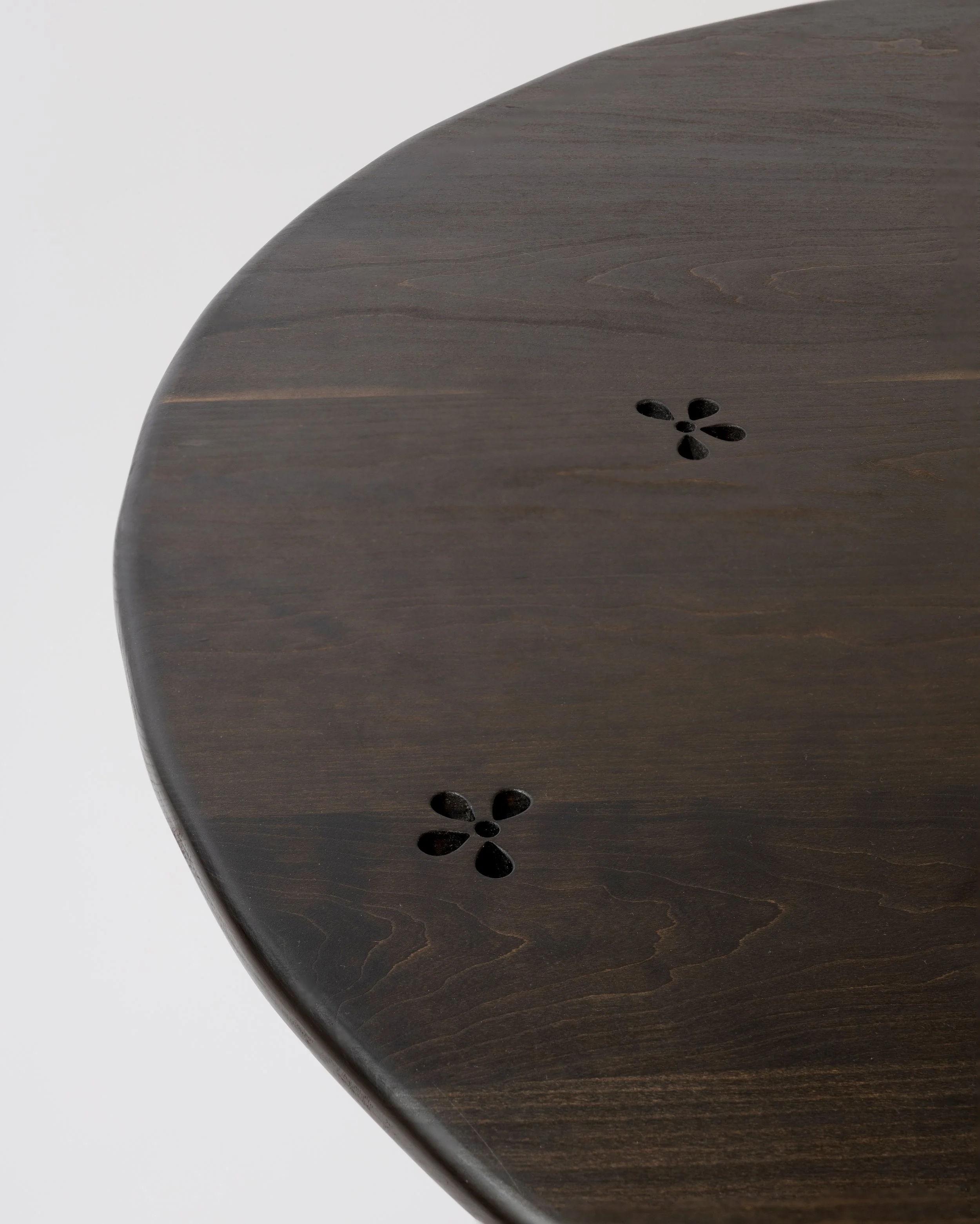 Close-up of a dark wooden round table with decorative carved flower patterns near the edges, against a plain white background.