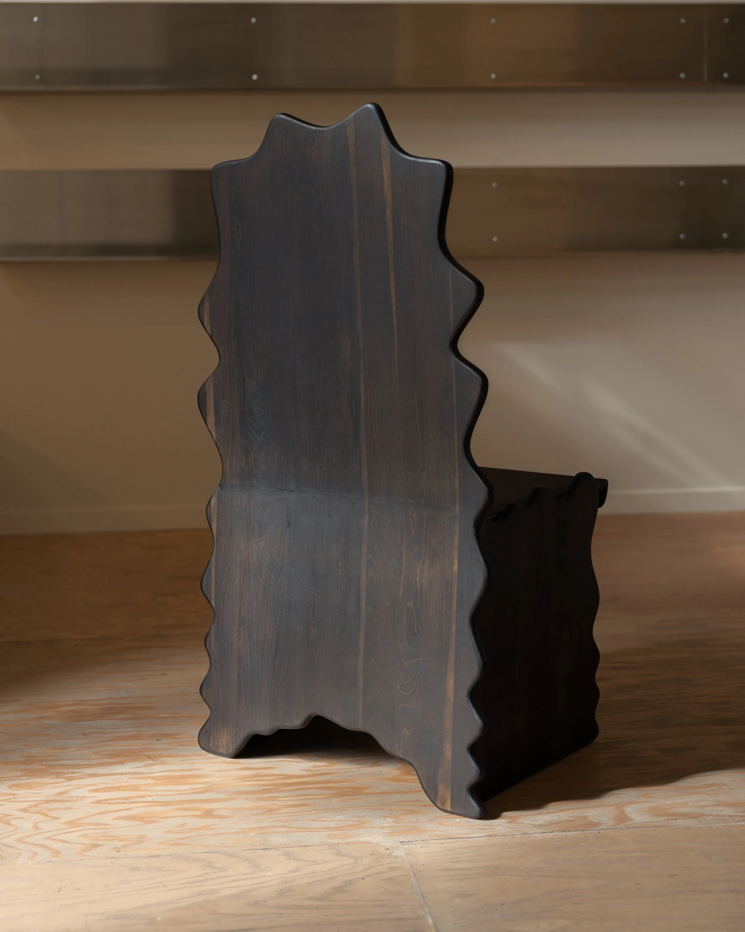 A dark wooden star-shaped object with wavy edges, standing upright on a wooden surface, casting a shadow.