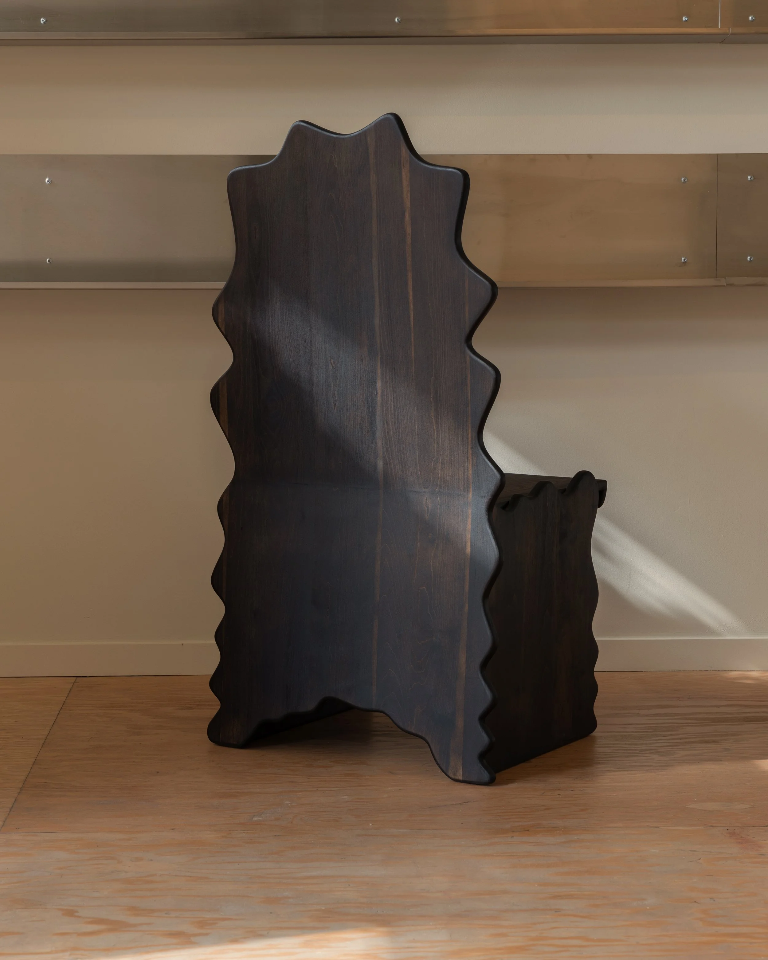 Dark wooden trolley with a unique wavy shape, positioned on a wooden floor against a beige and brown paneled wall.