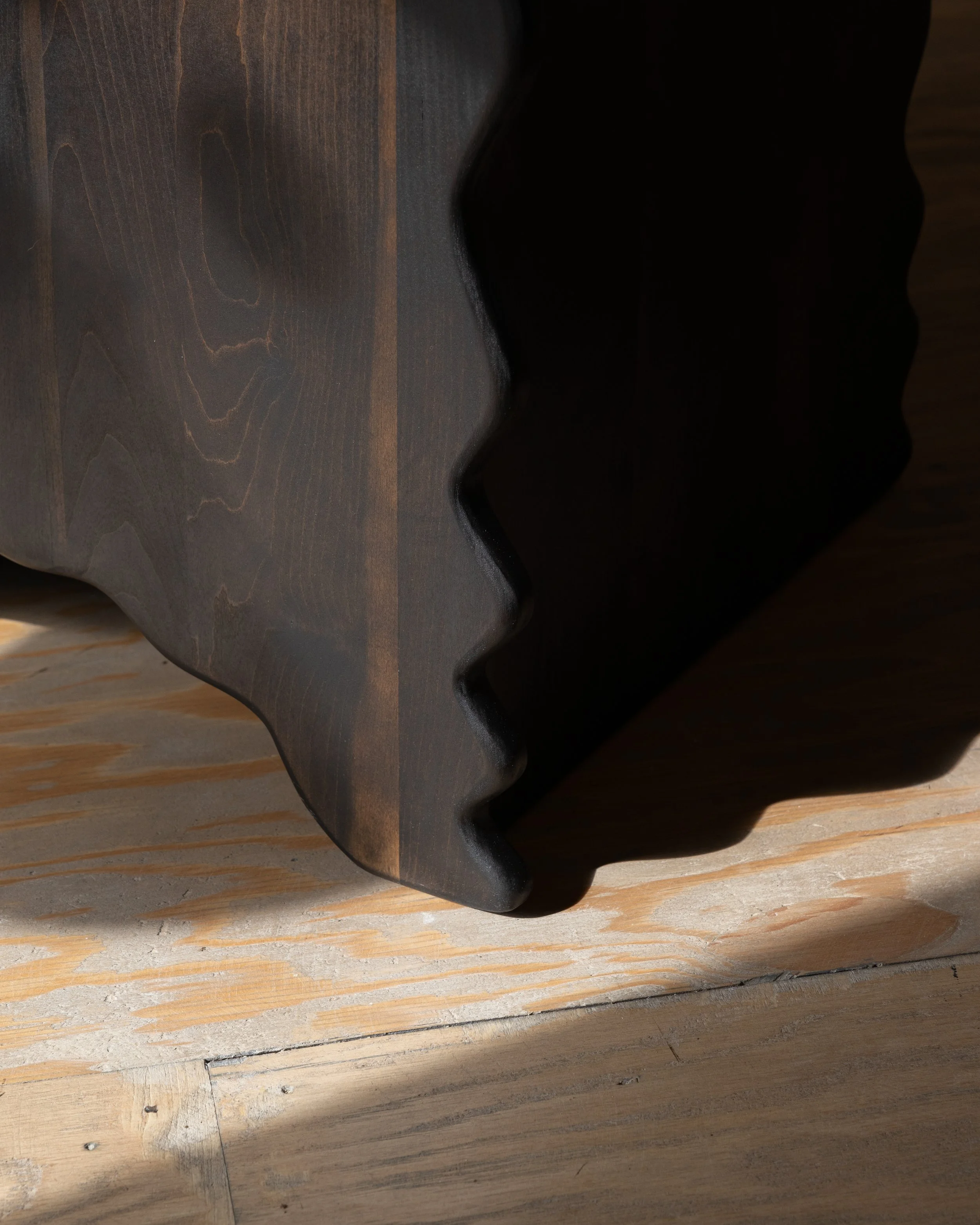 Close-up of a carved wooden sculpture with a smooth, dark finish, resting on a light-colored wooden surface.