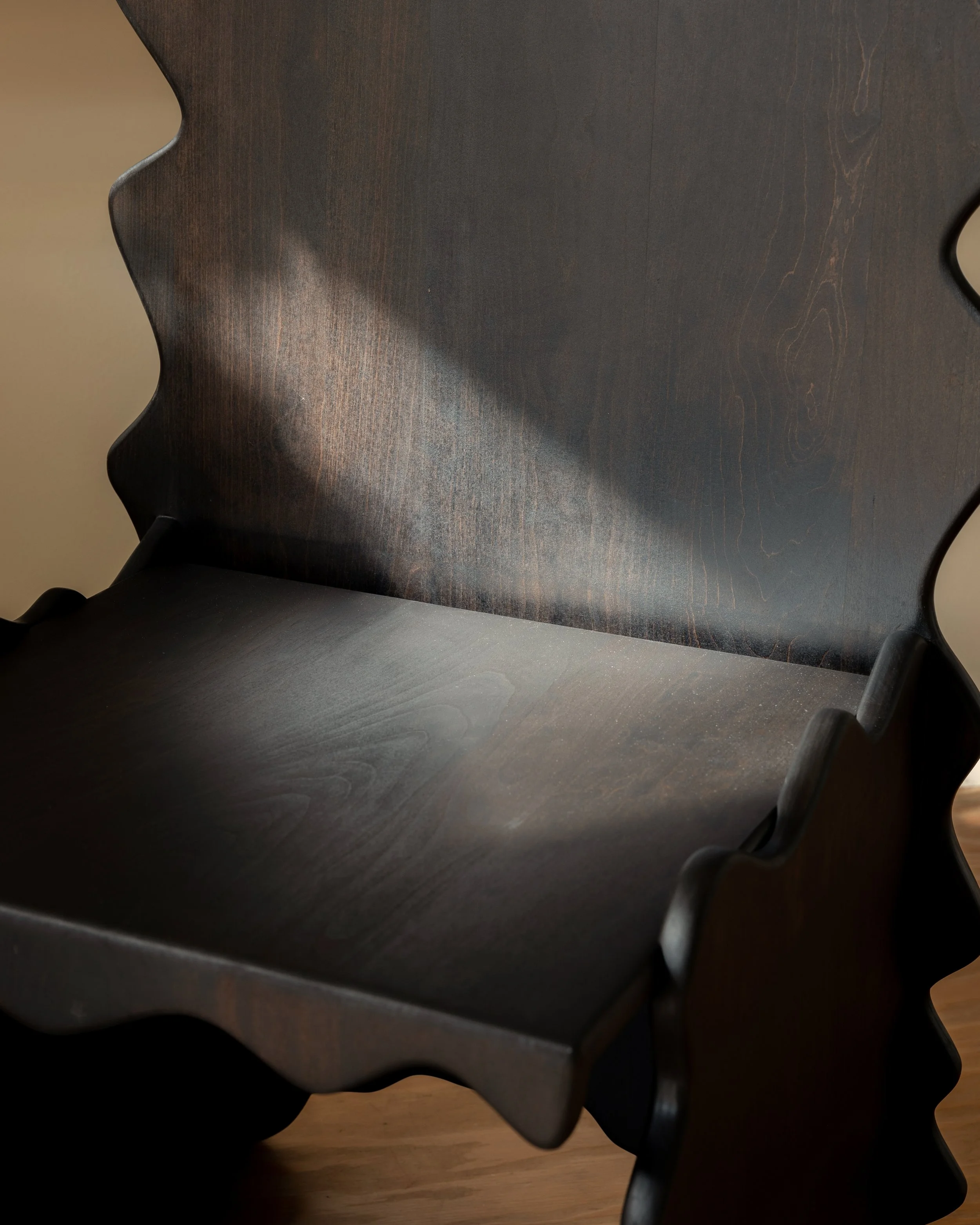 Close-up photo of a dark wooden chair with a carved backrest and curved armrest, with a wooden floor visible in the background.