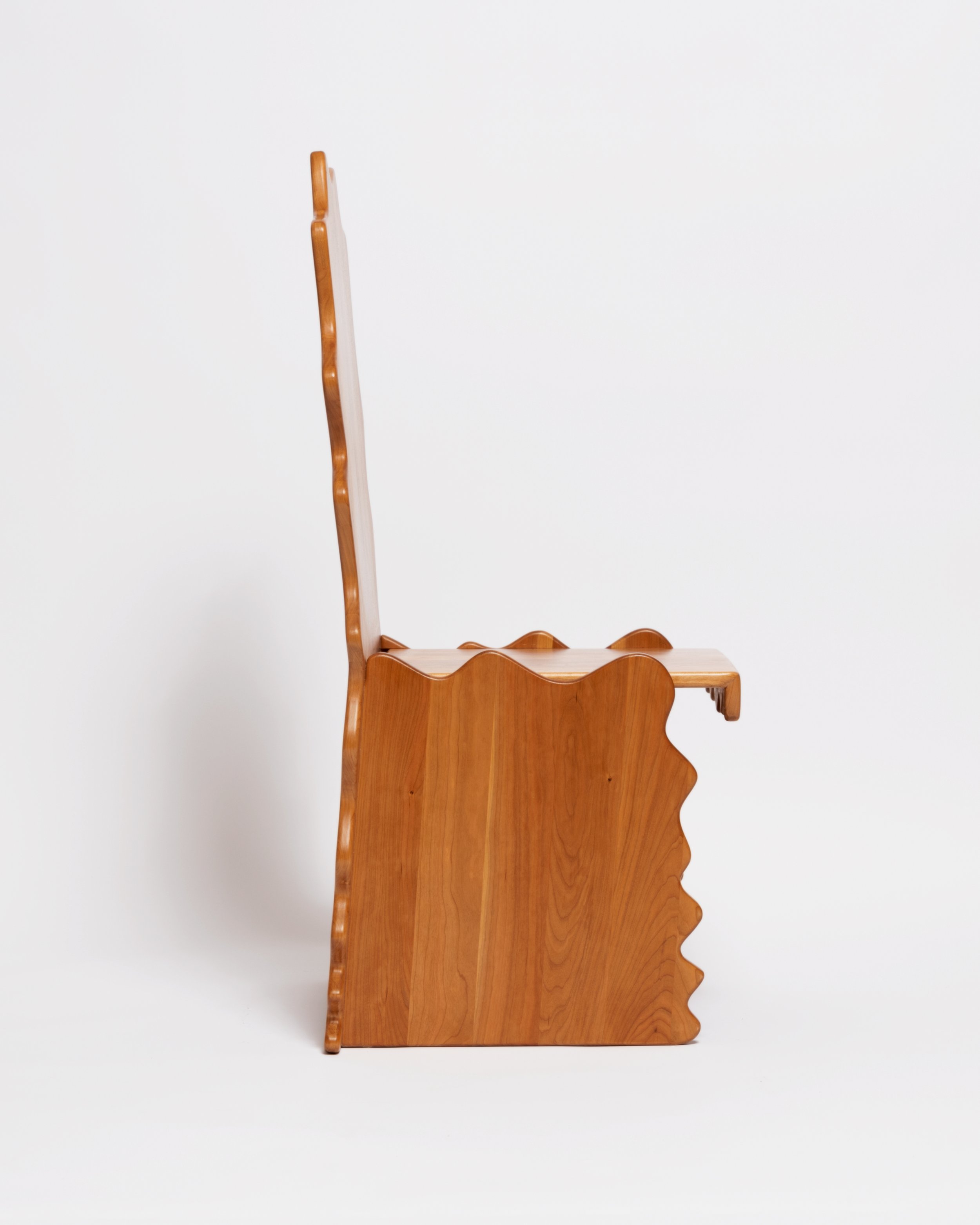 Wooden coat rack with a scalloped edge and a tall, curved arm against a plain white wall.