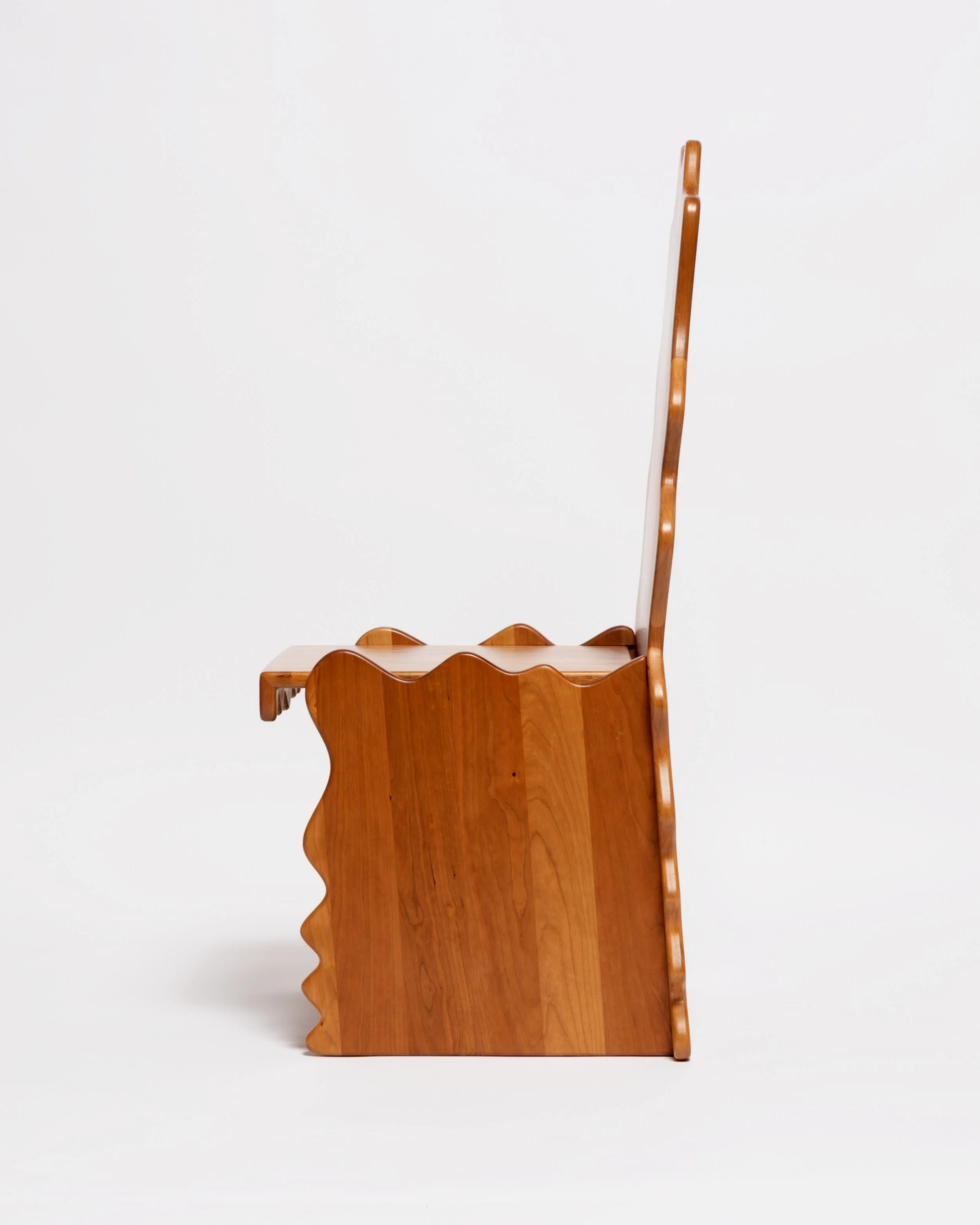 A wooden high chair with a scalloped edge on the tray, shown from the side, placed against a plain white background.