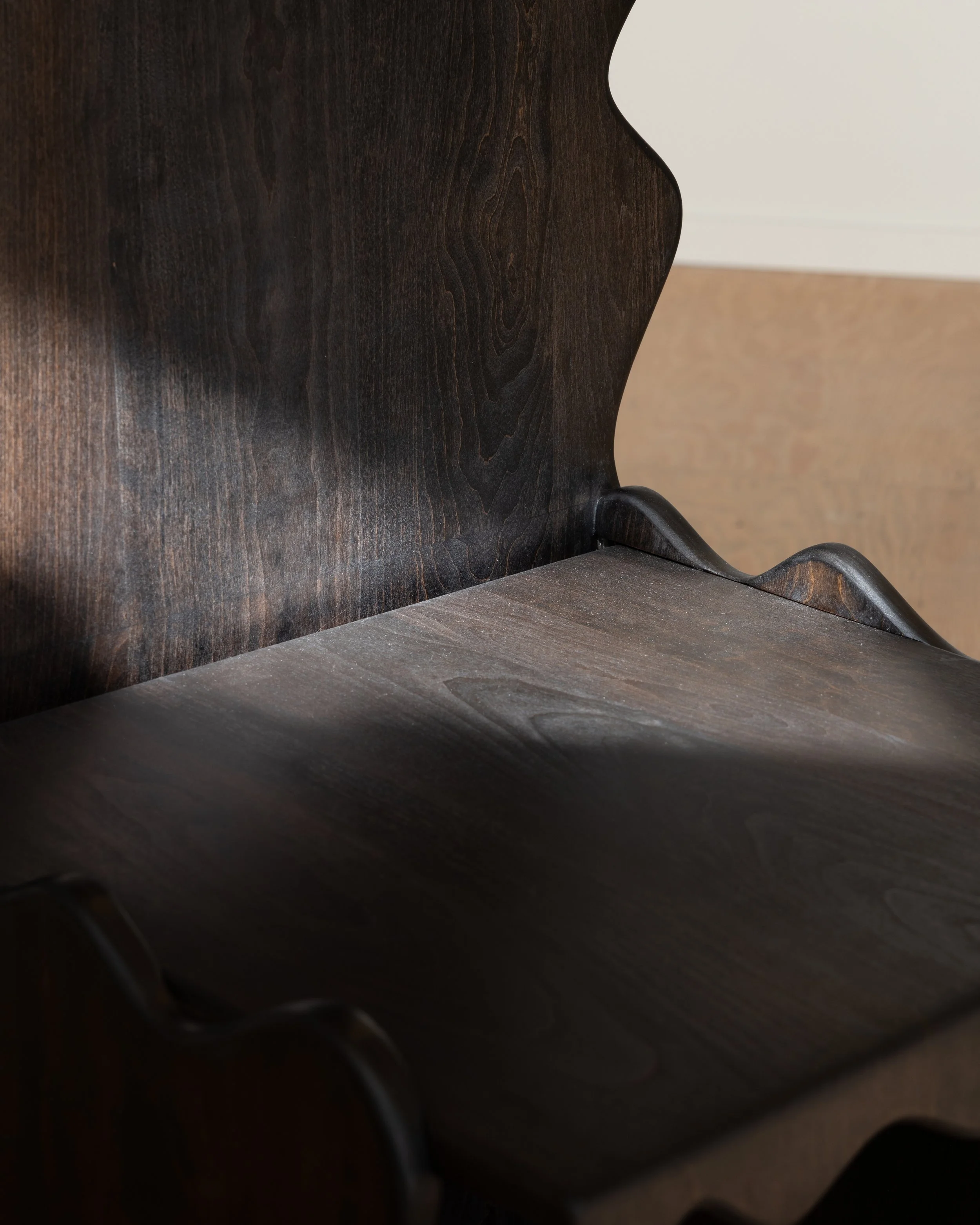 Close-up of a dark wooden chair with curved armrest and backrest, set against a beige-colored wall and a white baseboard.