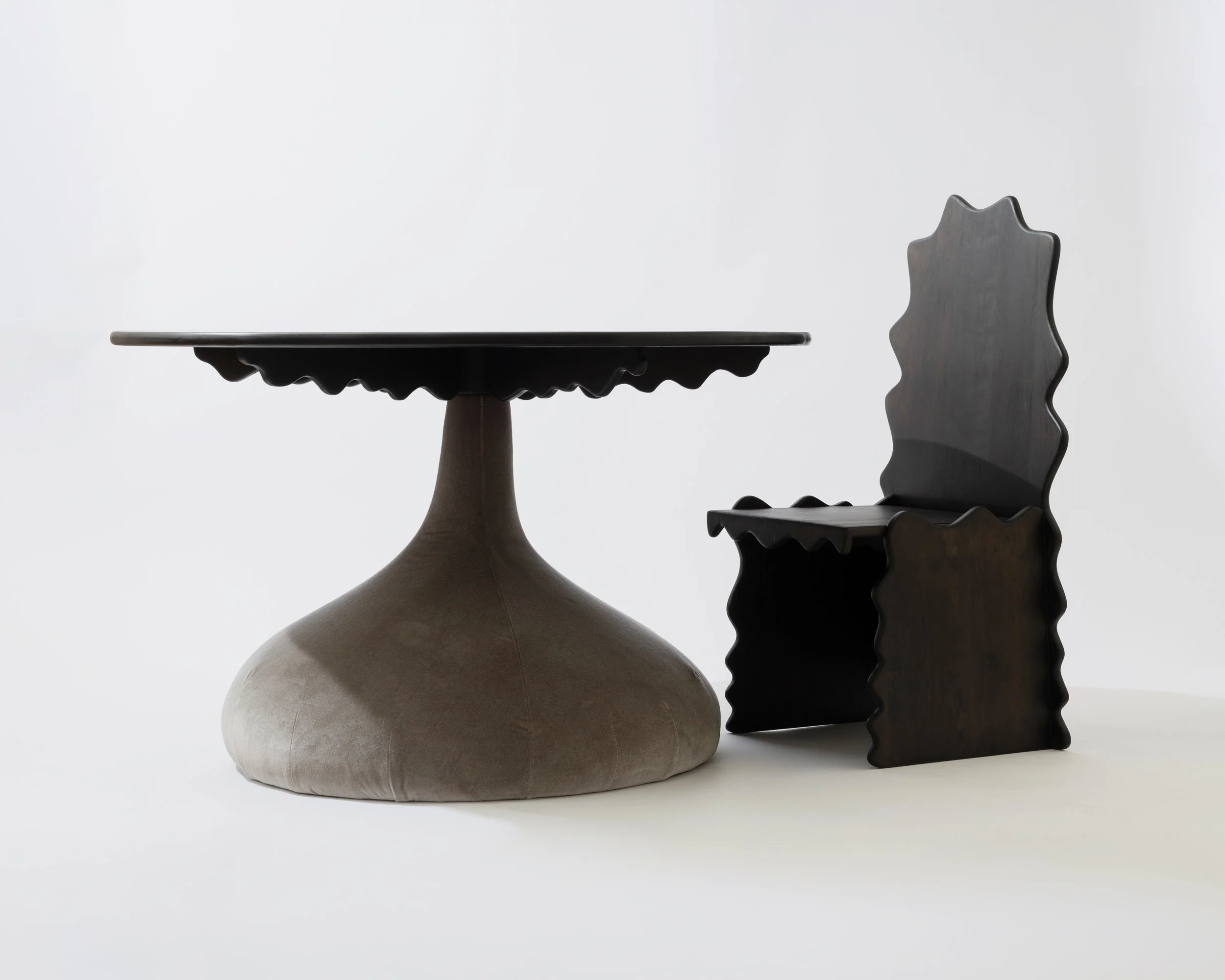 A ceramic vase, a black wooden table with a carved edge, and a wooden chair with a carved backrest are arranged on a white background.