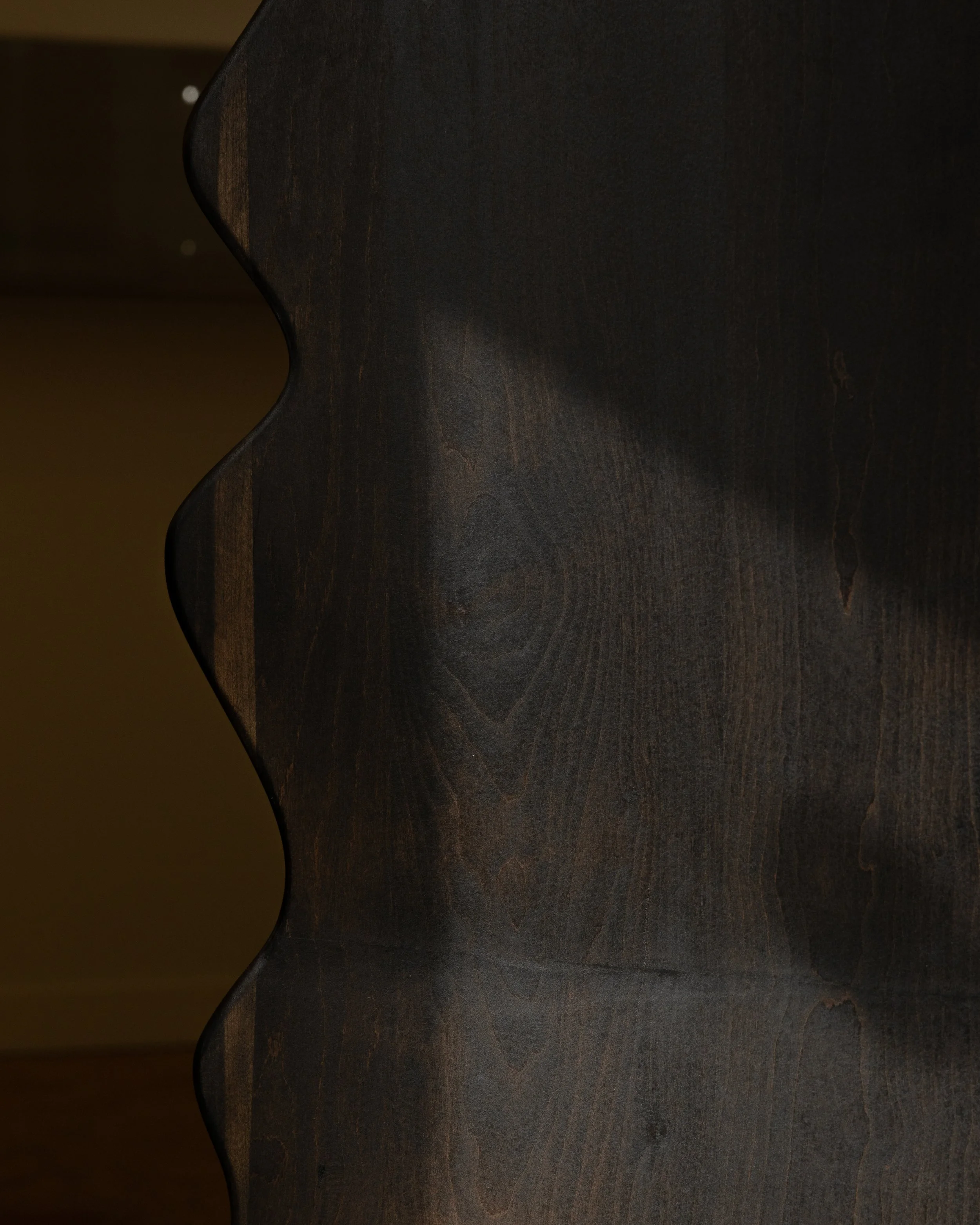 Close-up of a dark wooden furniture piece with a curved edge, showing wood grain and texture.