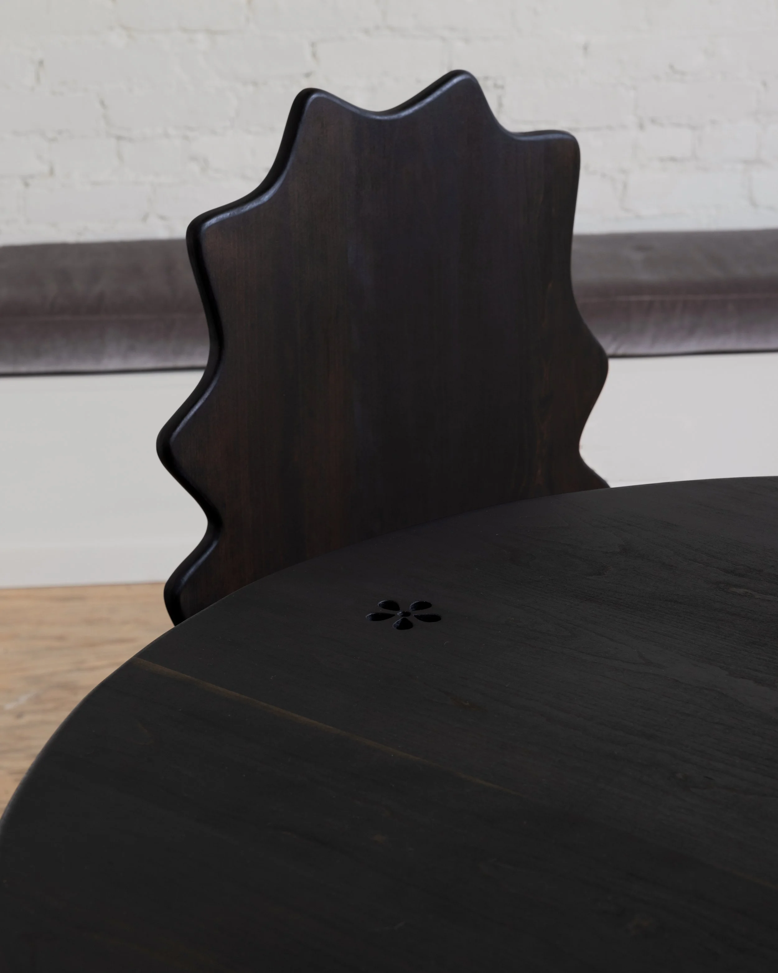 Close-up of a dark wooden chair with a backrest featuring a scalloped design, set against a plain wall with a horizontal wooden trim.