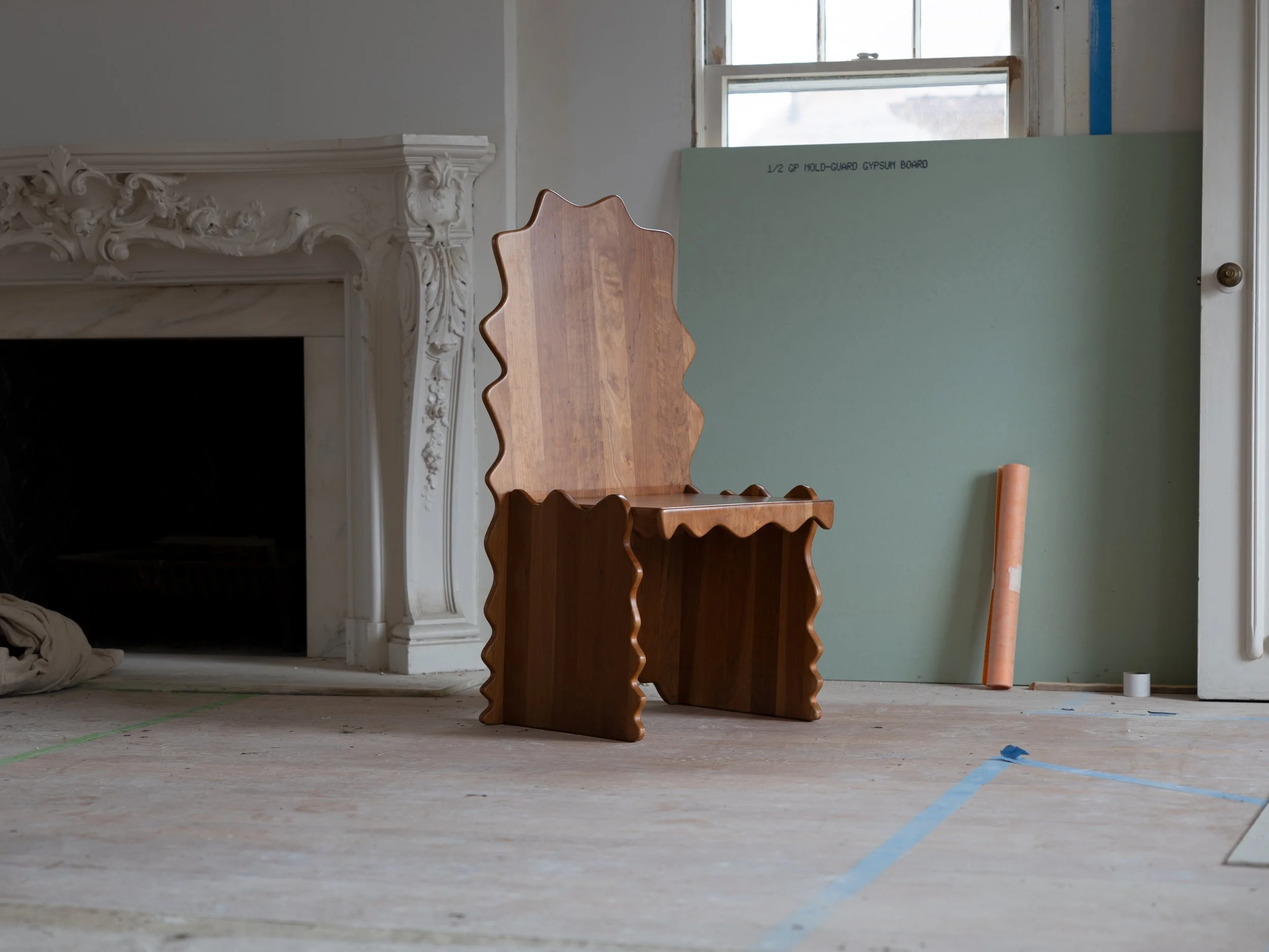Interior room under construction with a wooden chair, green drywall panel, and construction tools on a bare floor.