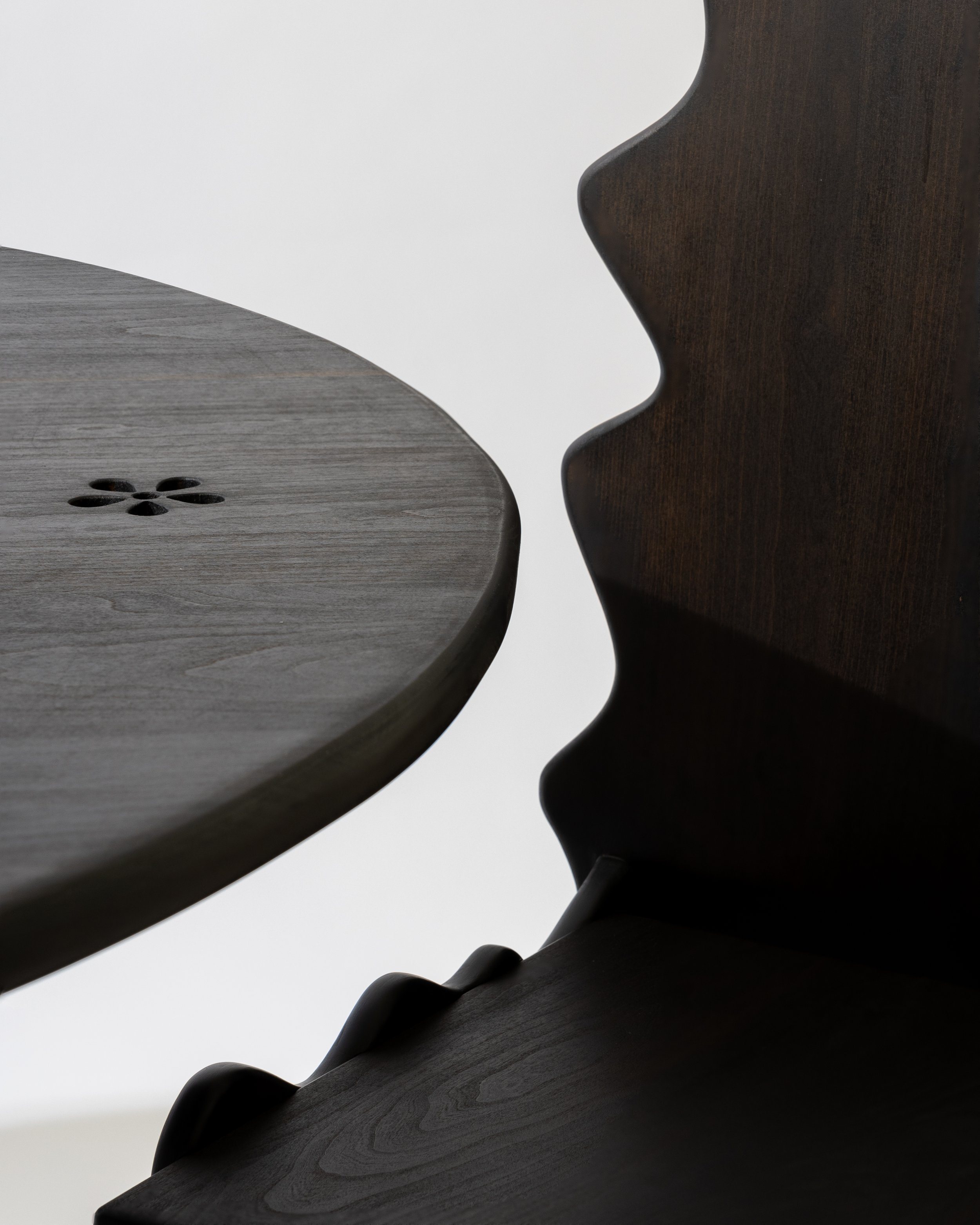 Close-up of two dark wooden furniture pieces with distinct shapes, one with a flower-shaped hole pattern, against a plain white background.