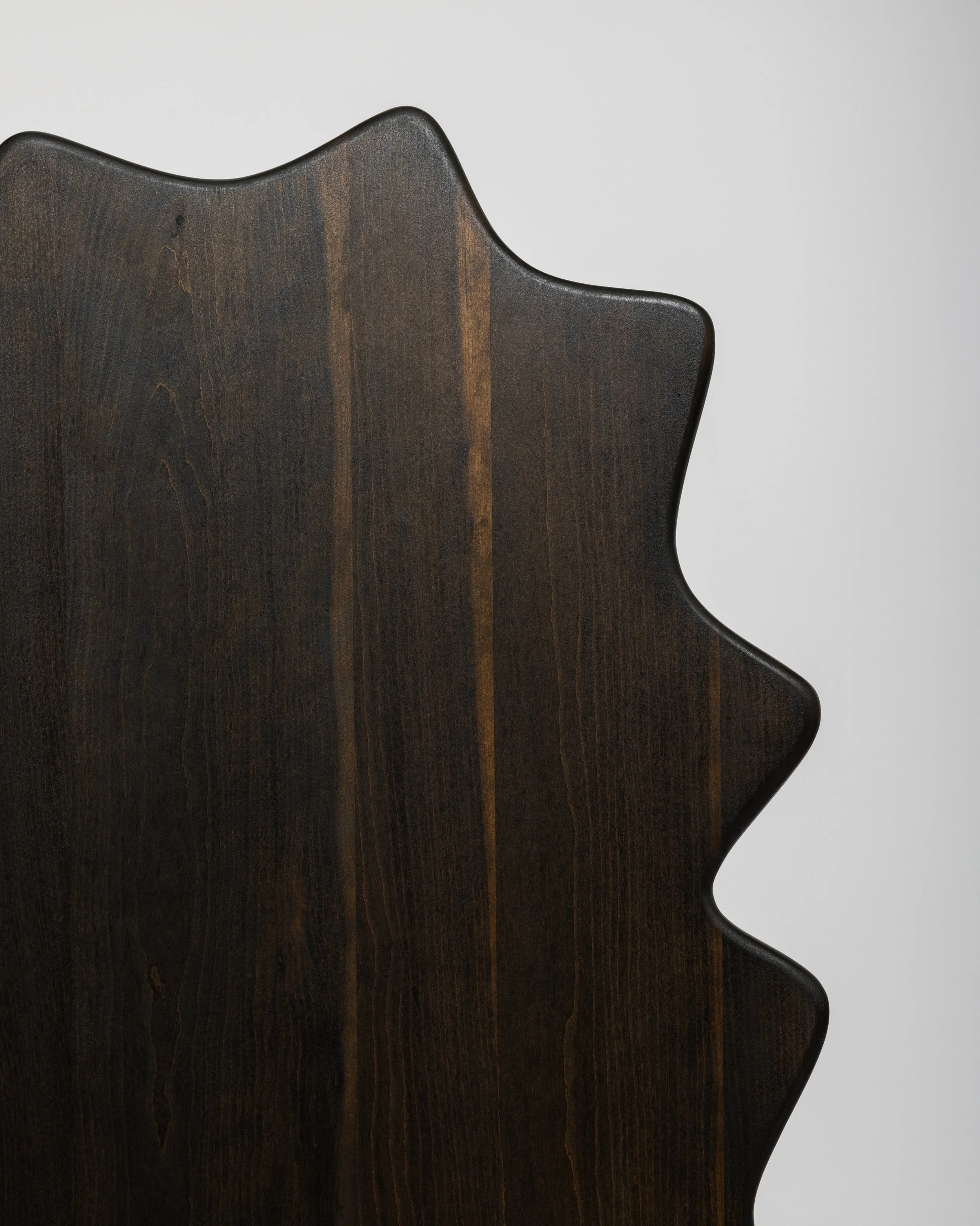 Close-up of a dark wooden chair back with a curved shape, set against a plain gray wall.