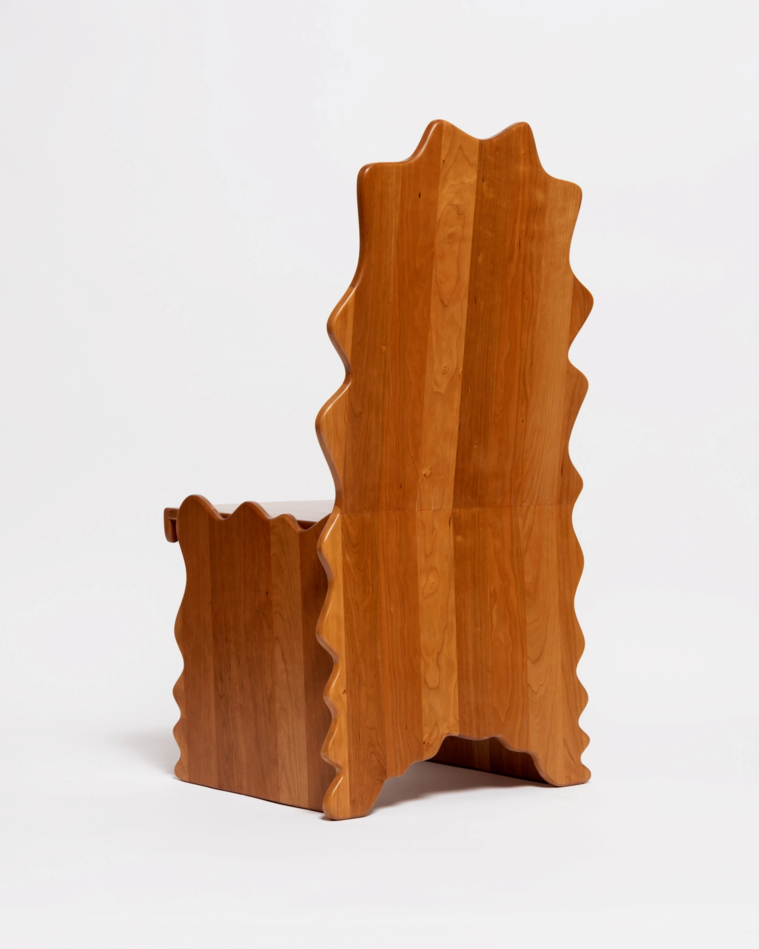 Close-up of a decorative wooden chair with a jagged, leaf-like silhouette against a plain white background.