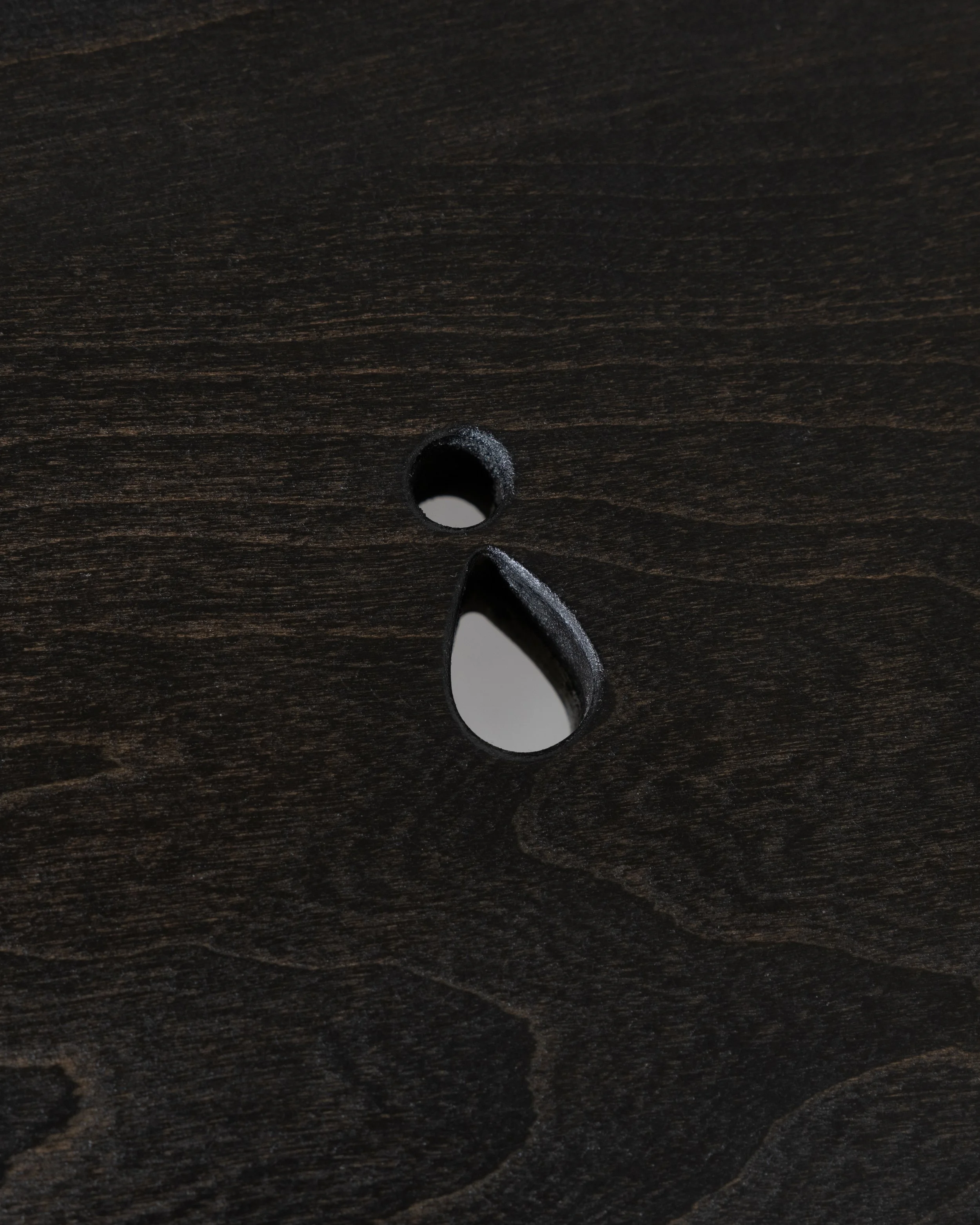 Close-up of dark wooden surface with a single round hole and a curved groove beneath it.