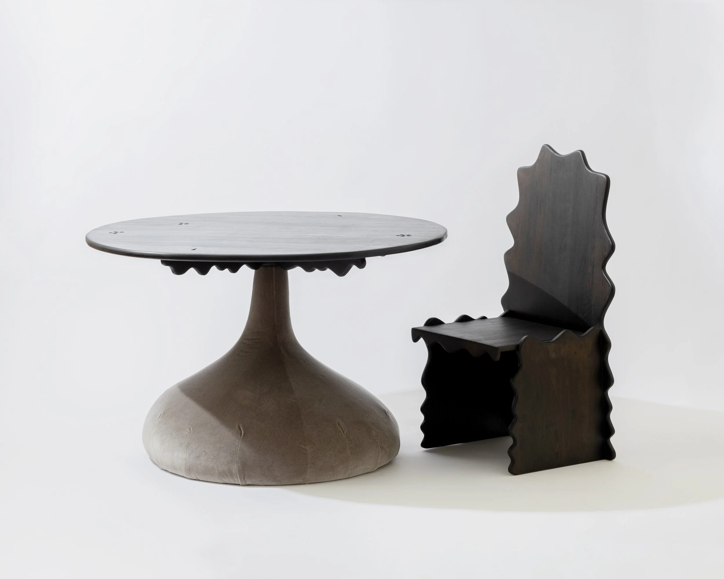 A round pedestal table with a beige cushion and a wooden chair with a cloud-shaped backrest against a plain white background.