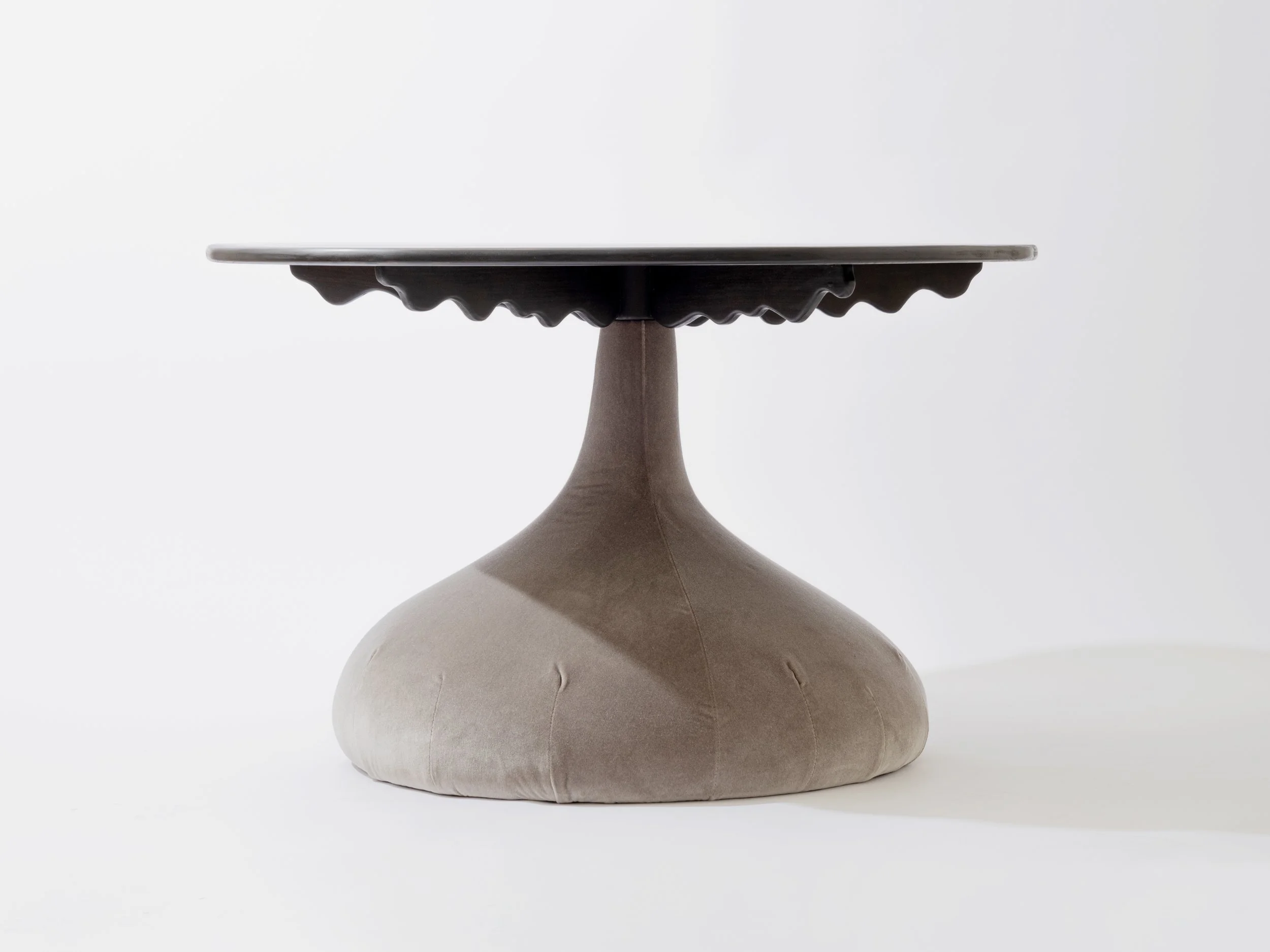 A beige and dark brown sculptural object with a rounded base, a slender neck, and a circular, flat top surface, positioned against a plain, white background.