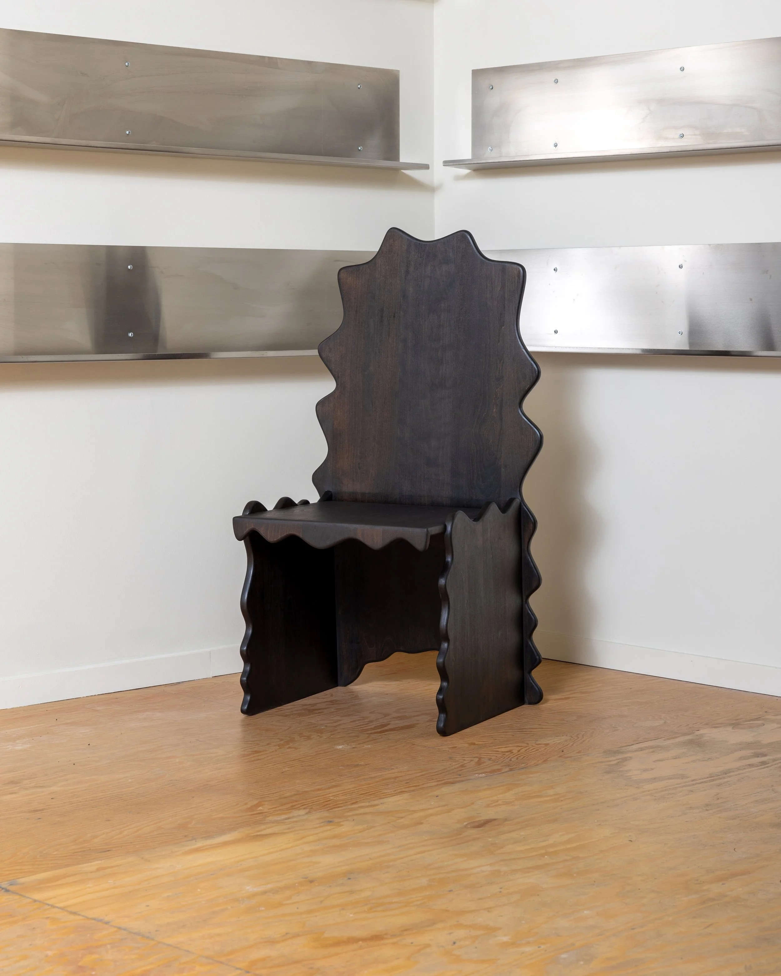 A dark wooden, scalloped-edge chair in front of a white wall with metal shelves.