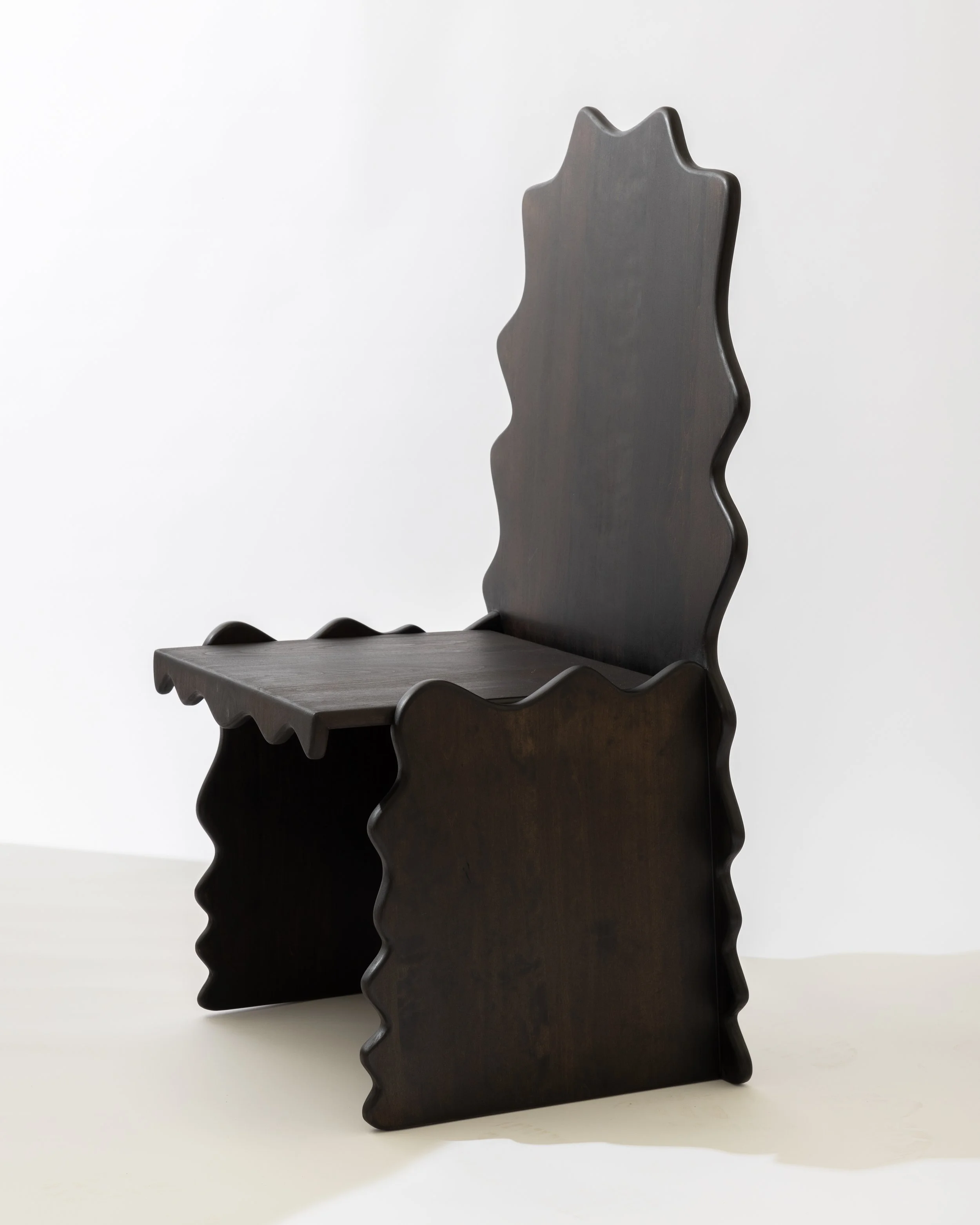 Three dark-colored wooden chairs with wavy backs and seats, positioned in front of a white background.