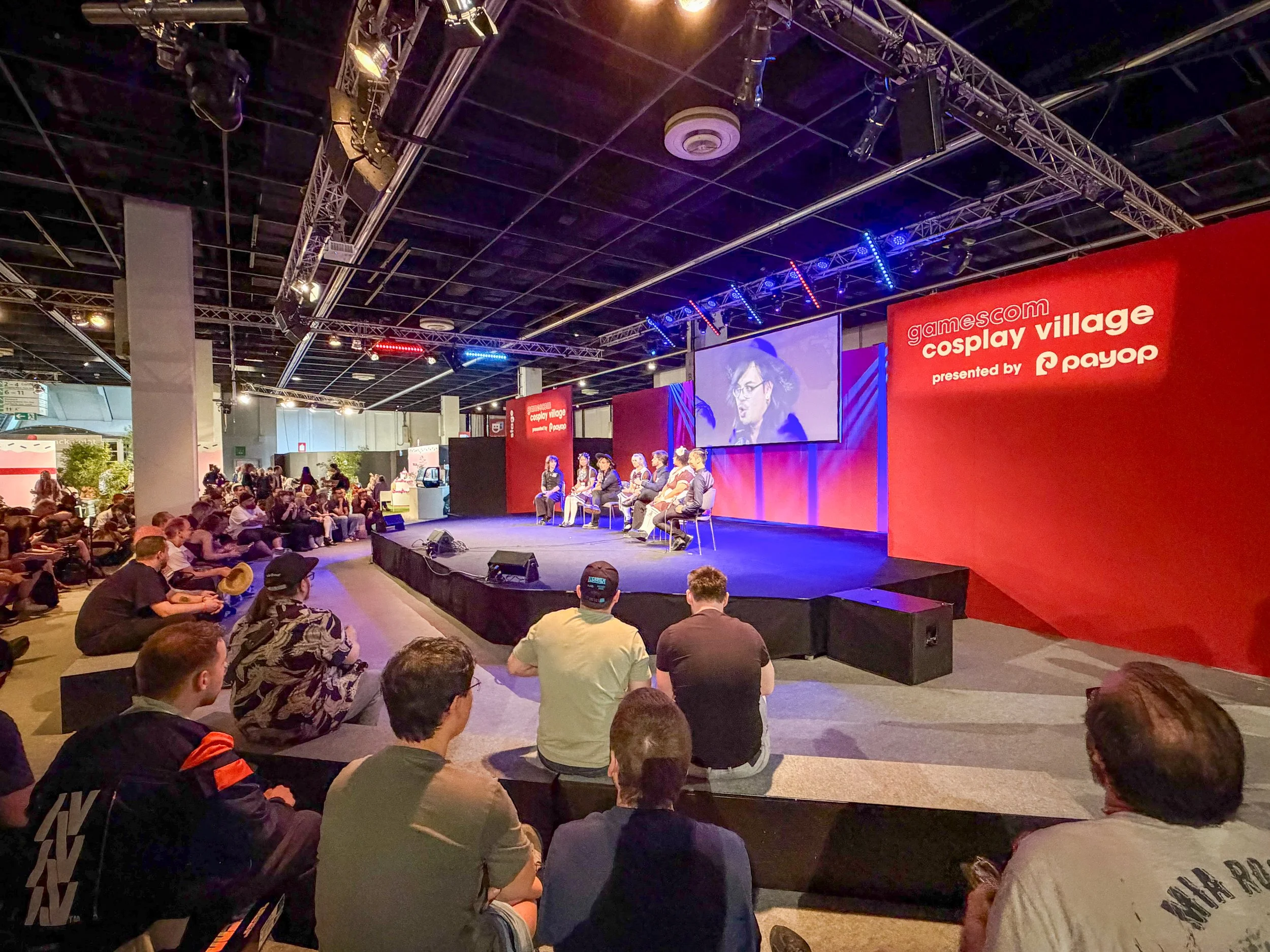Gamescom 2026 Cosplay Village with fans gathered around a live stage discussion, showing the community side of gaming culture
