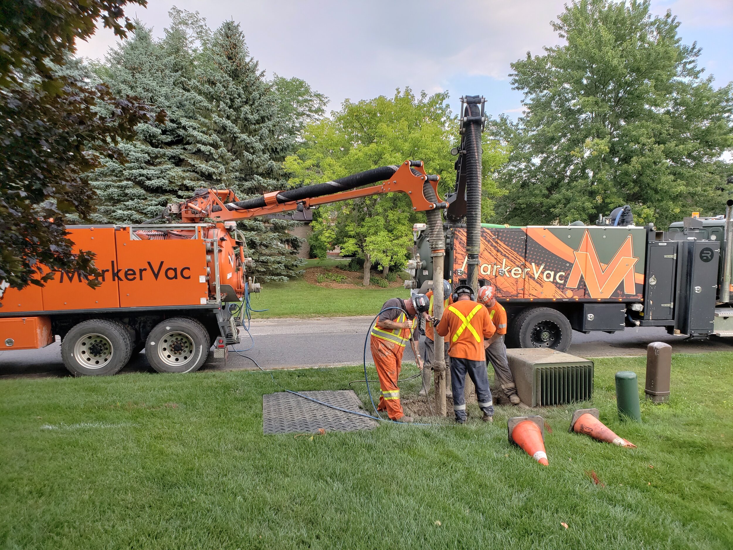 Workers in safety gear operating a hydrovac truck for excavation near a grassy area.