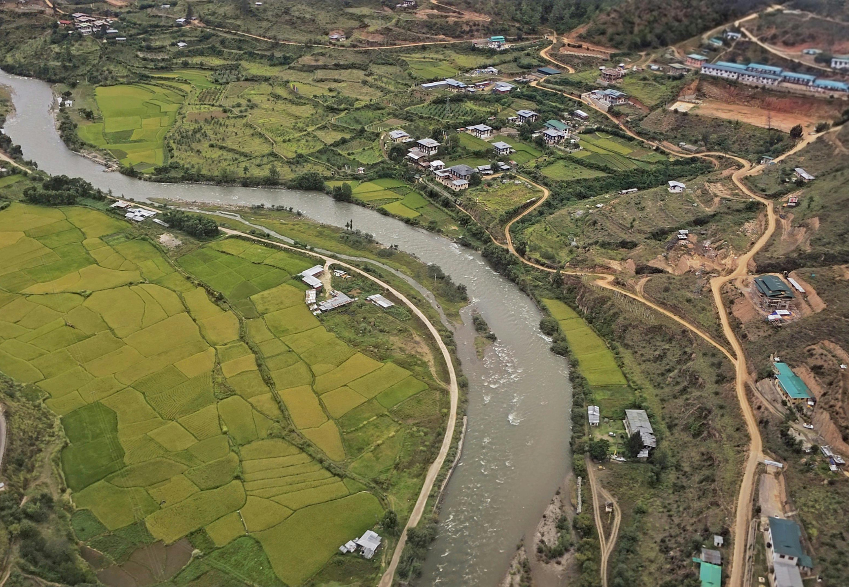 Aerial view of a river flowing through a green landscape with a city in the background, clear blue sky.