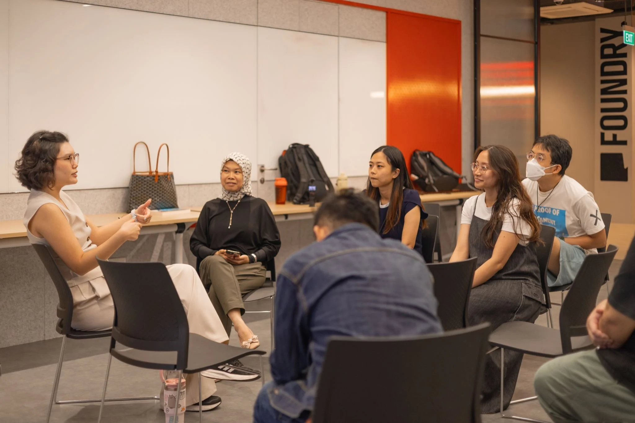 Xin Yi seated in a circle, speaking with the participants listening attentively.