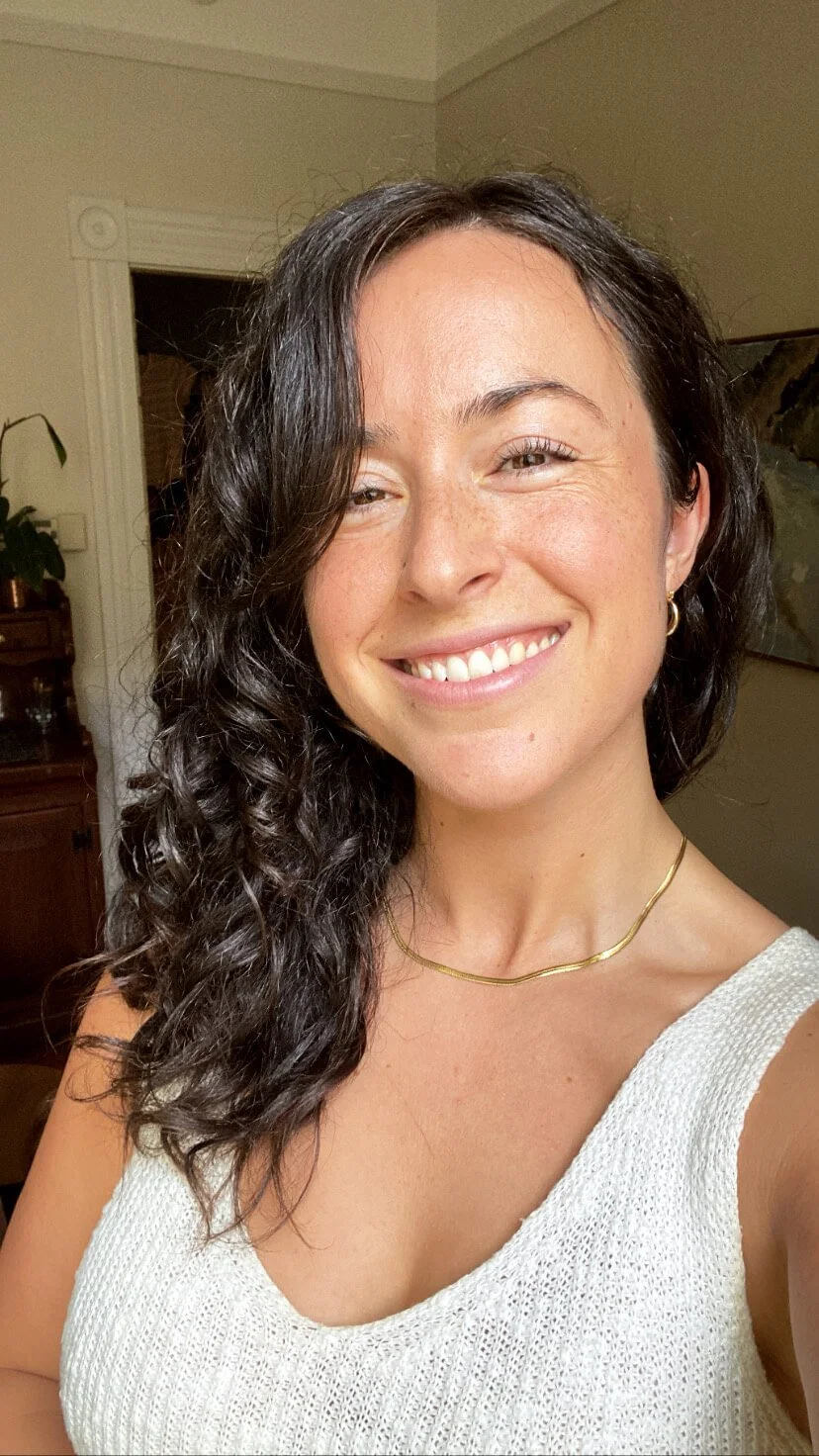 A woman with dark, curly hair smiling in a well-lit room.