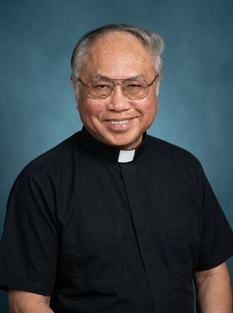 Portrait of a smiling man wearing glasses and a black clerical shirt with a white clerical collar, against a blue background.